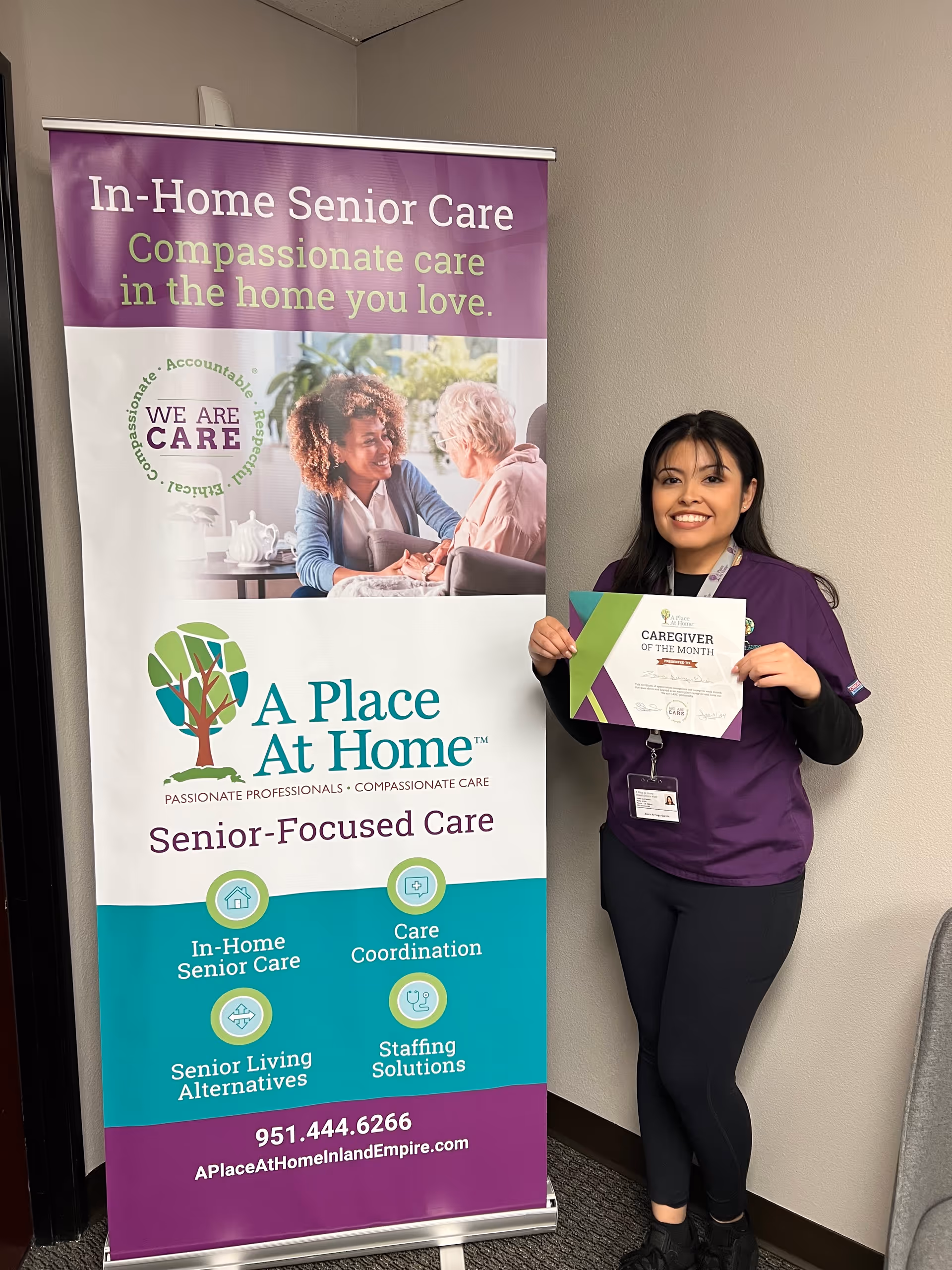 Caregiver posing beside a promotional banner for A Place at Home Inland Empire.