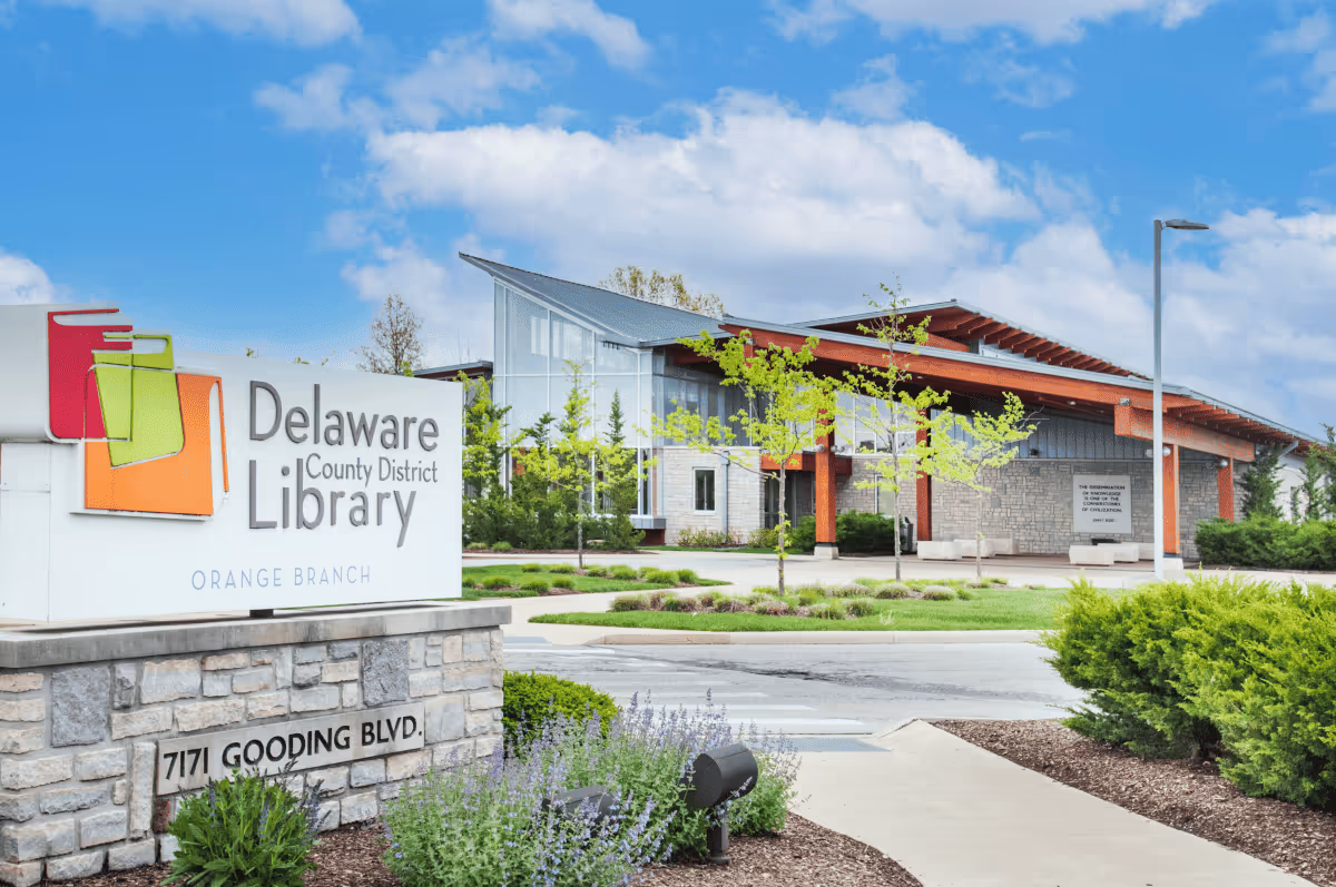 Exterior view of a modern library building with a stone sign and landscaping.