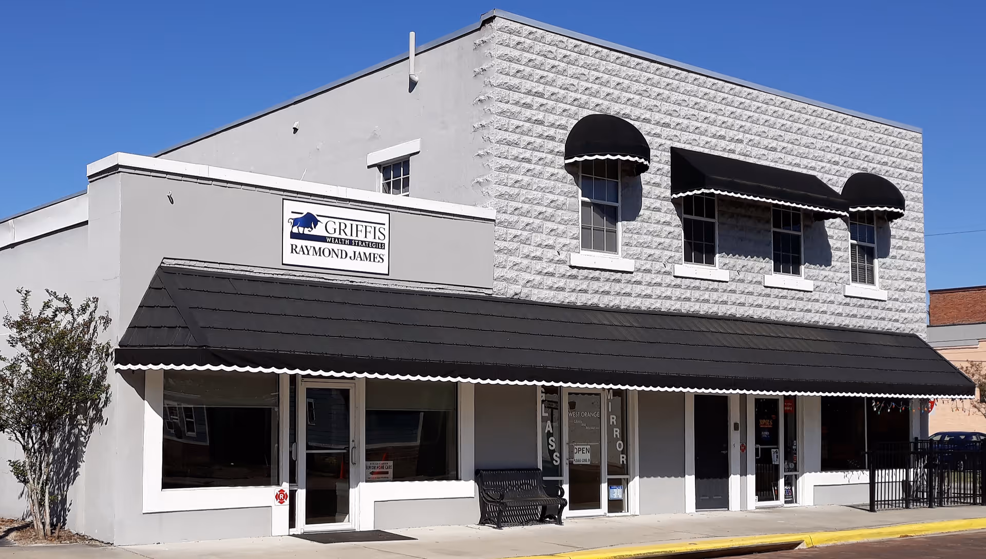 Exterior view of a two-story building with black awning, storefront windows, and a bench.