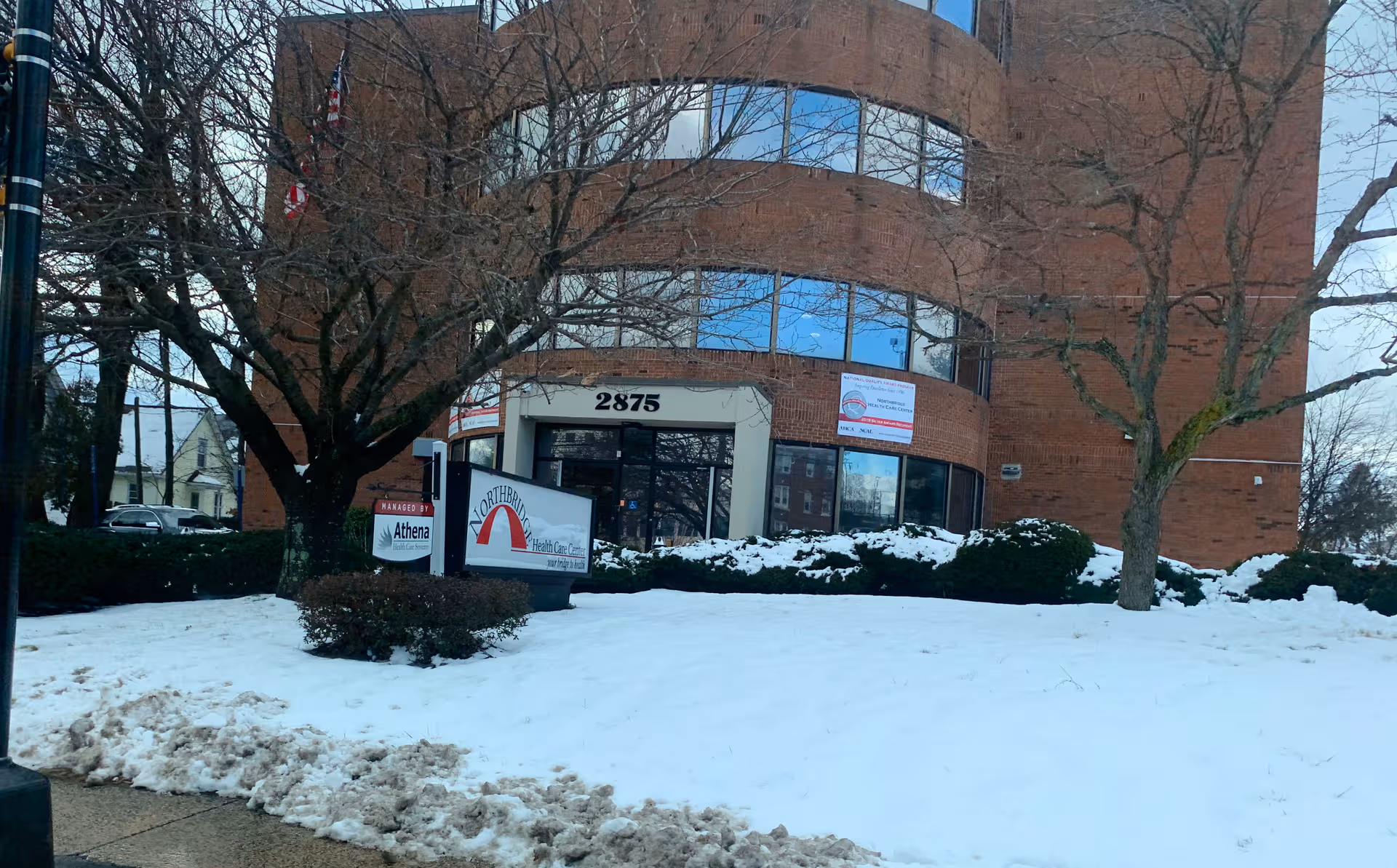 Brick health care center with rounded entrance, snow-covered lawn, and bare trees.
