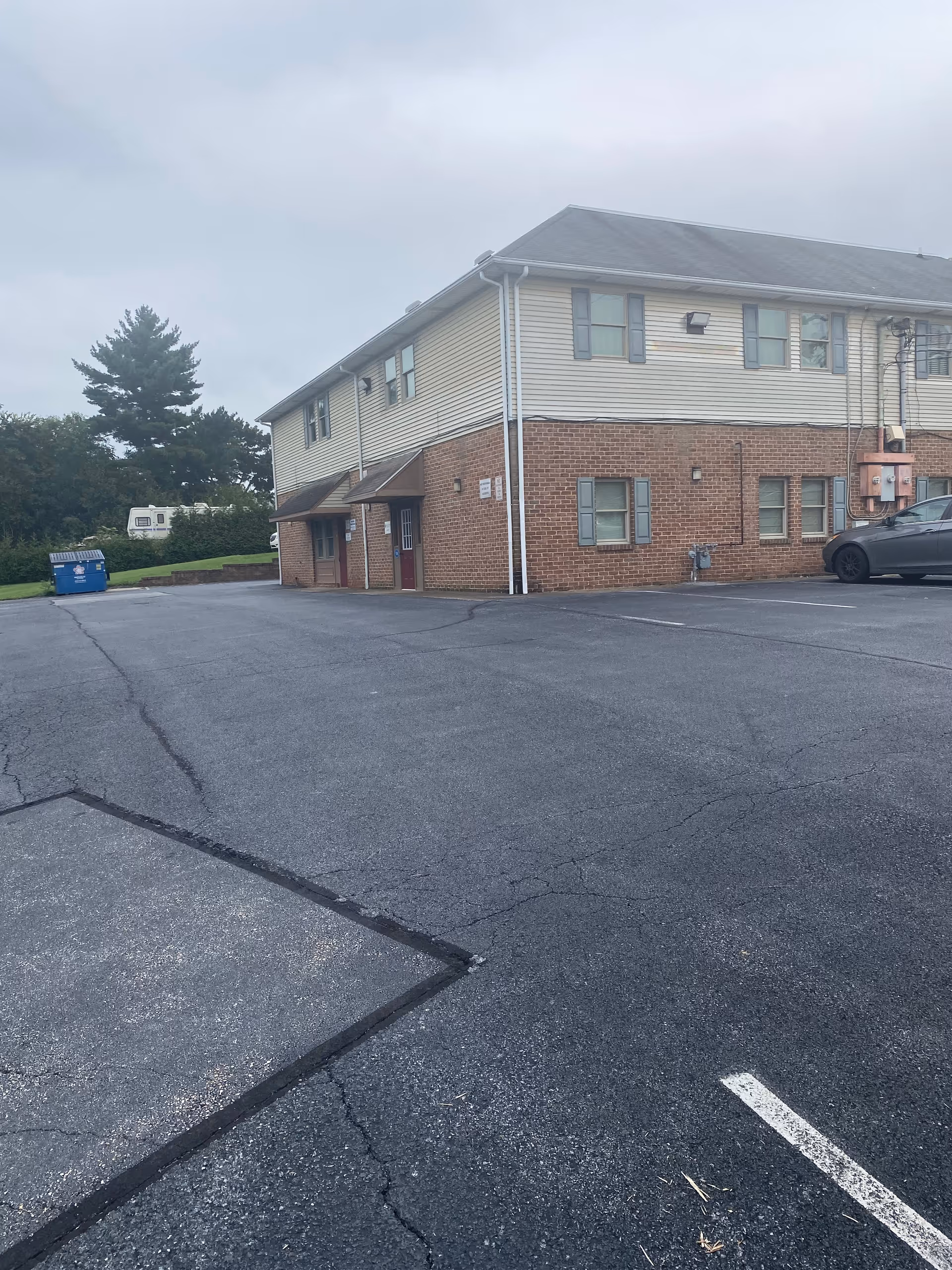 Two-story senior facility exterior with brick, beige siding, and a large parking lot.