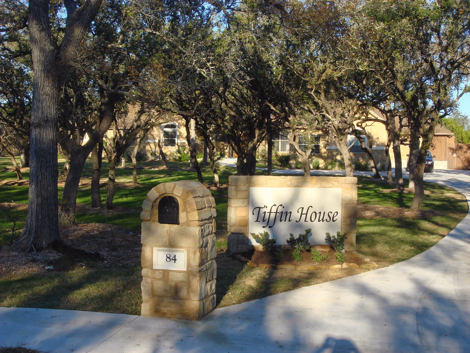 Stone sign reading Tiffin House at the entrance with curved driveway and trees.