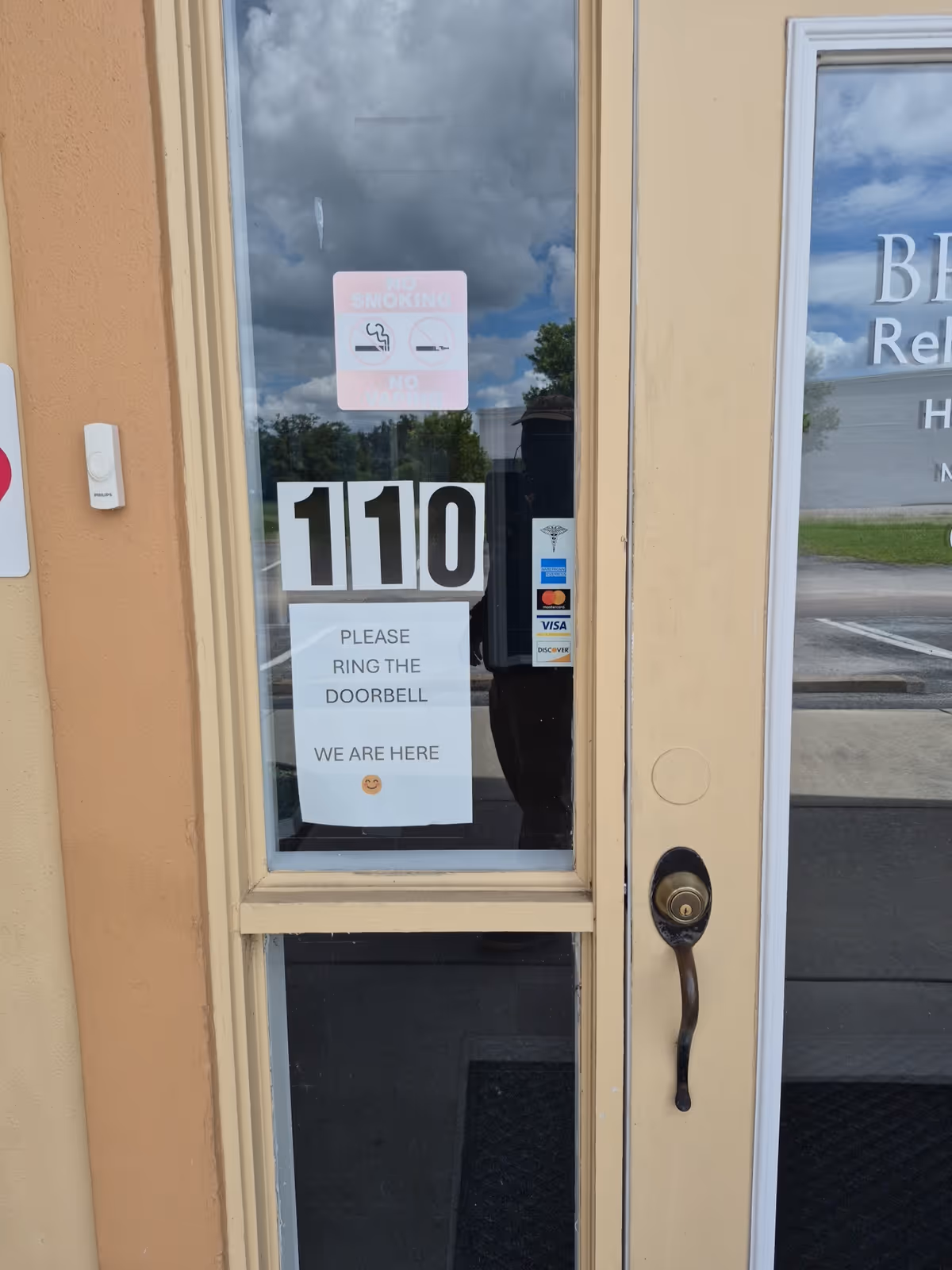 Glass door entrance with 110 numbers and signs asking to ring the doorbell.