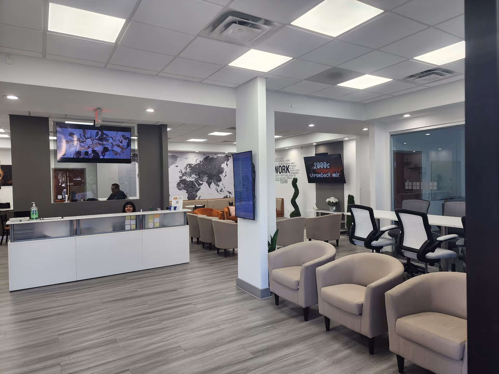 Modern reception area with a white desk, seating, and screens.