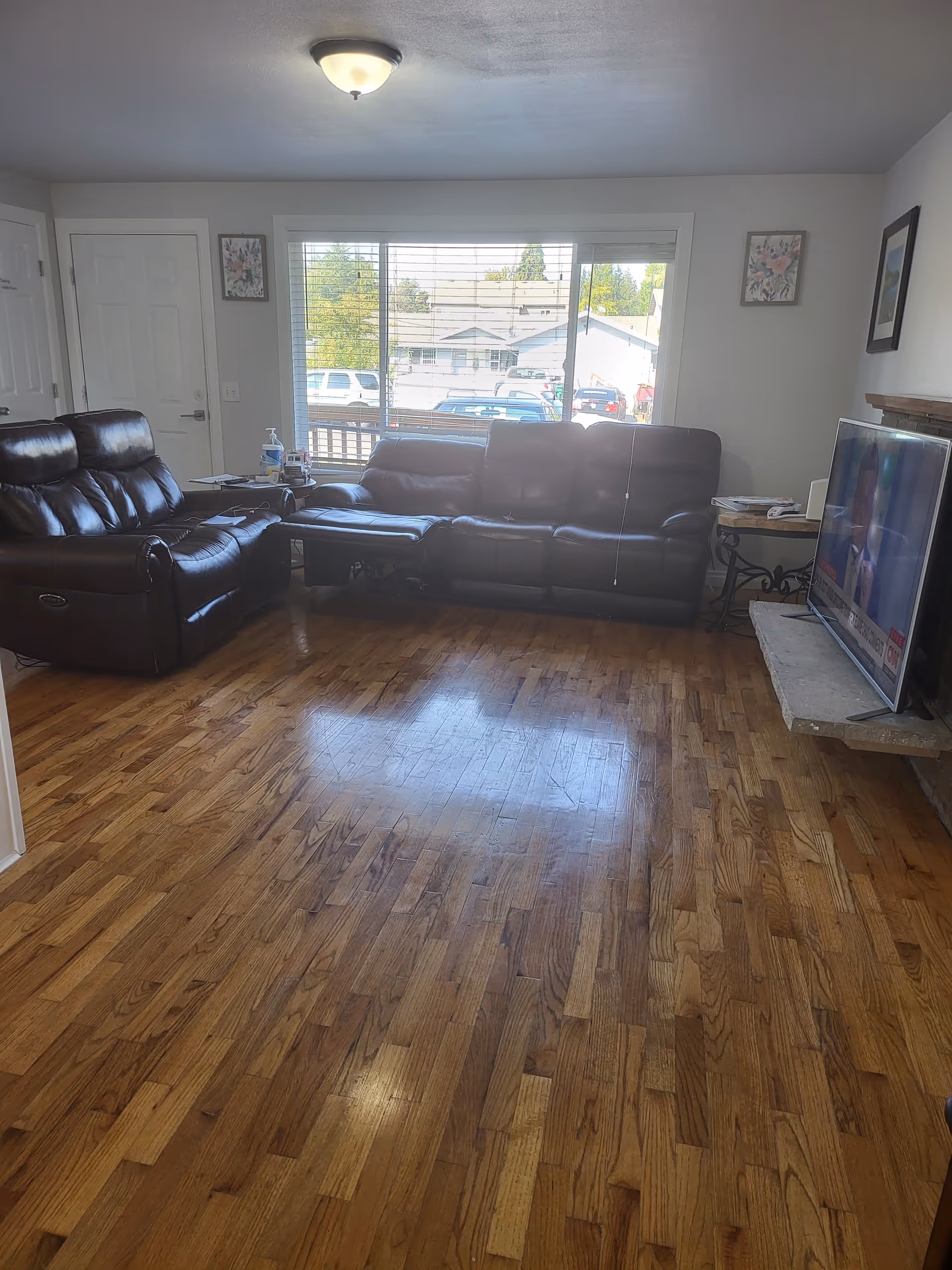 Living room with leather sofas, wood floor, TV, and large window.