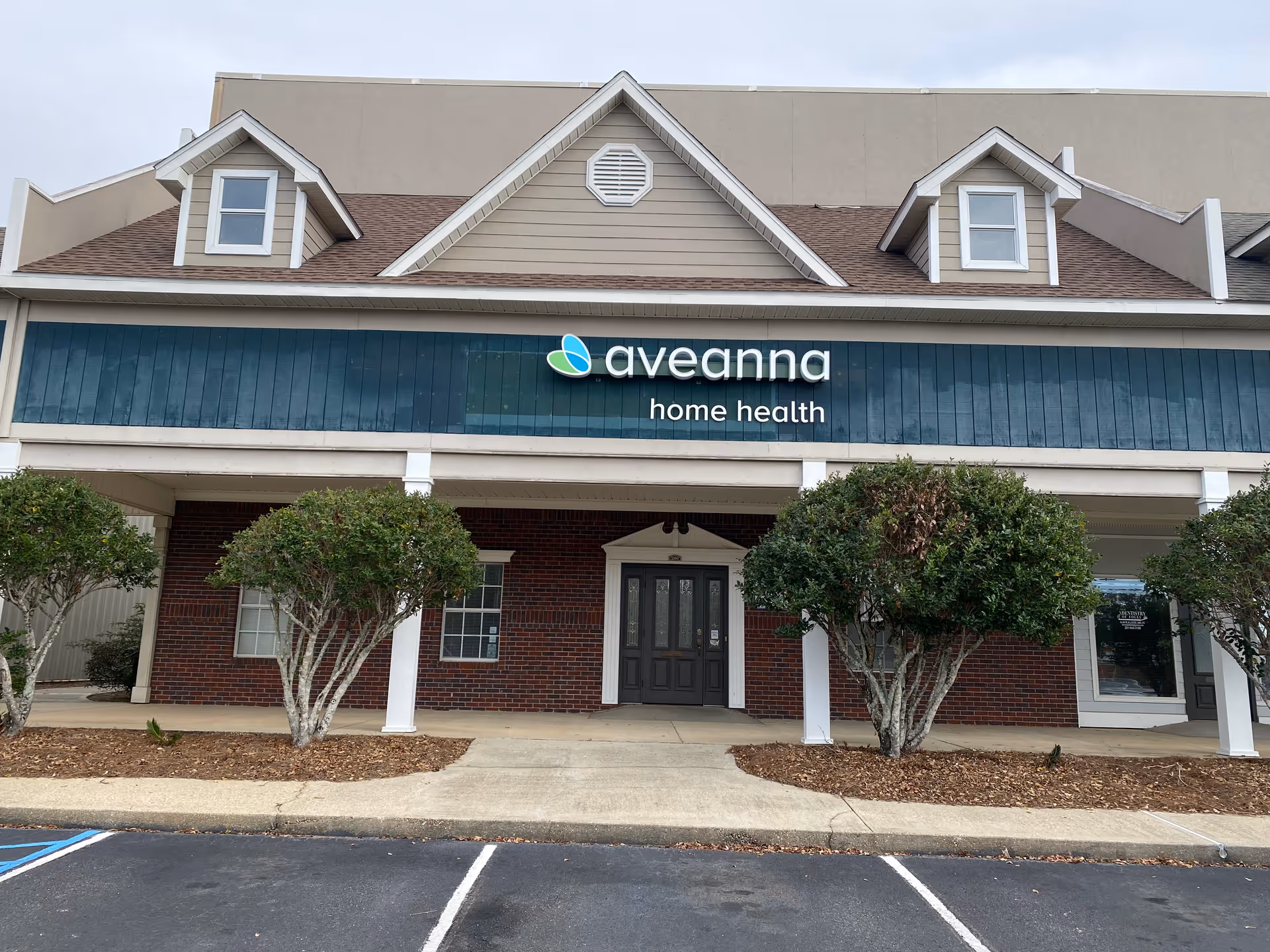 Exterior of Aveanna Home Health building with blue sign and trimmed shrubs.