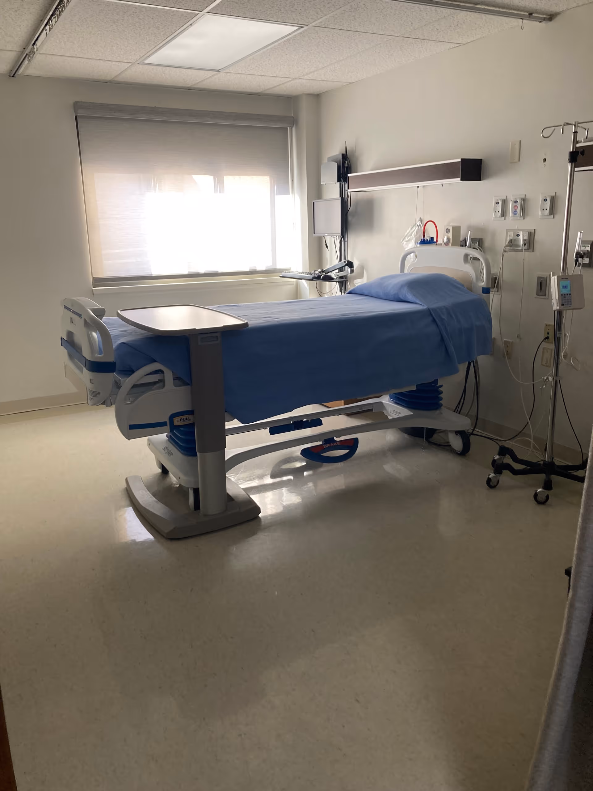 Hospital room with a blue sheet on an adjustable bed and medical equipment.