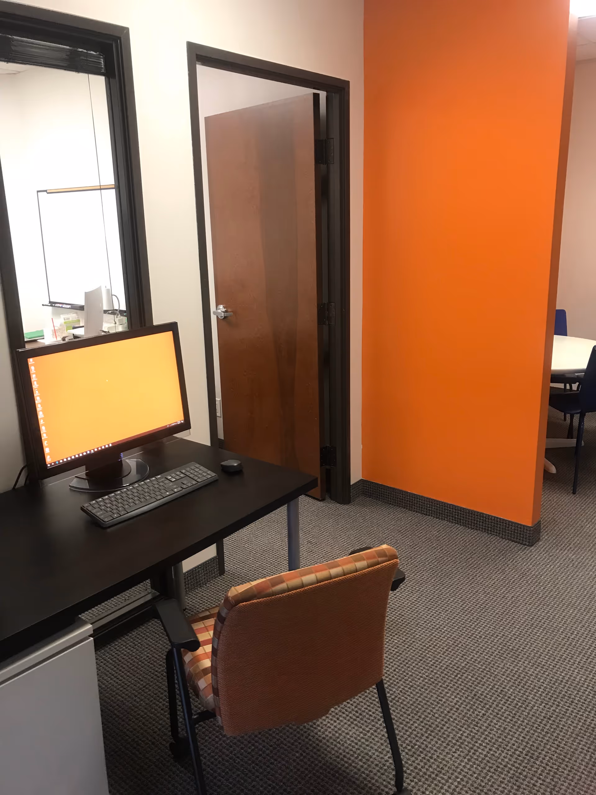 Desk with computer on a black desk beside an orange wall in an office.