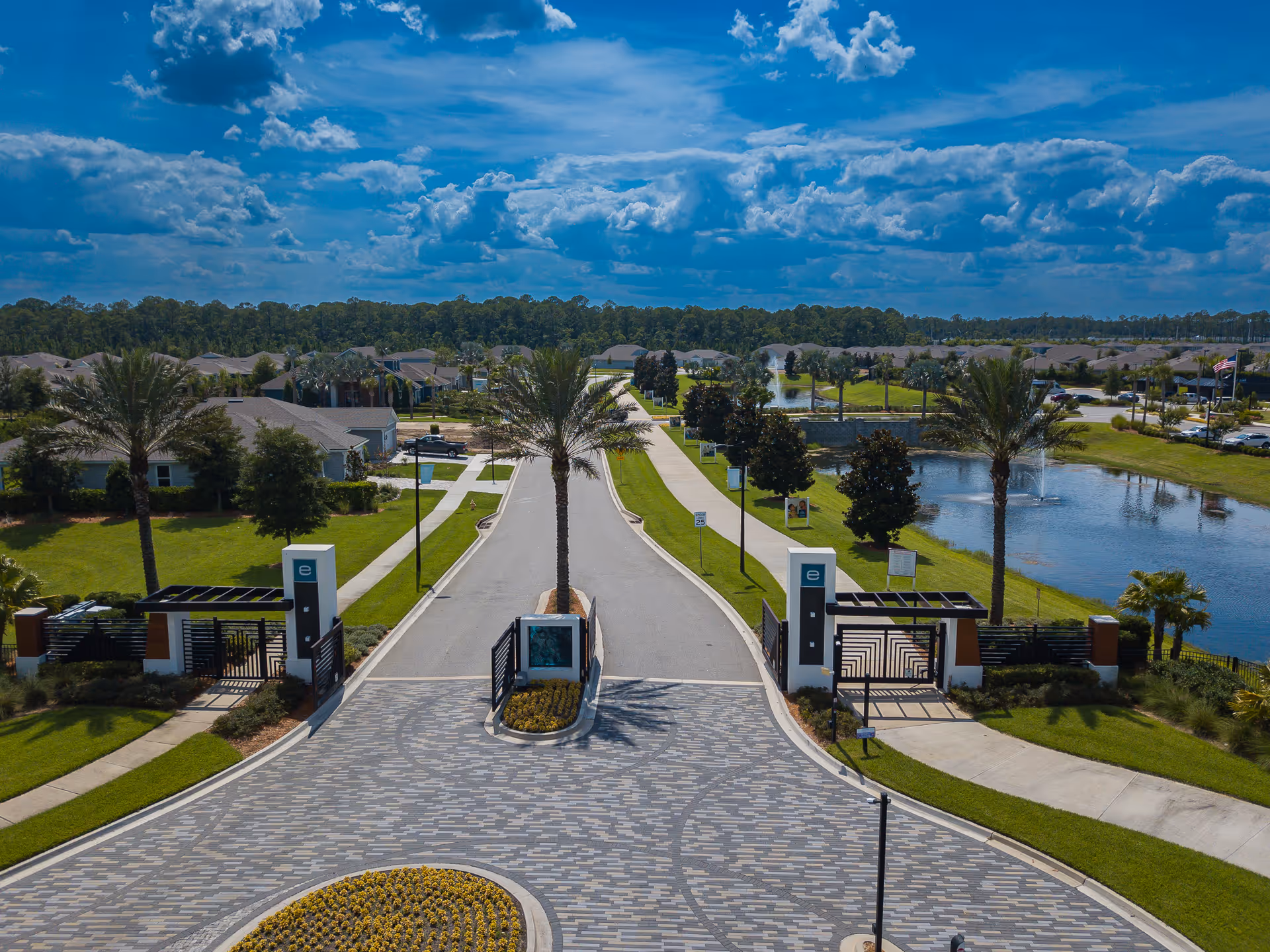 Aerial view of gated senior living community entrance with palm trees and a pond.
