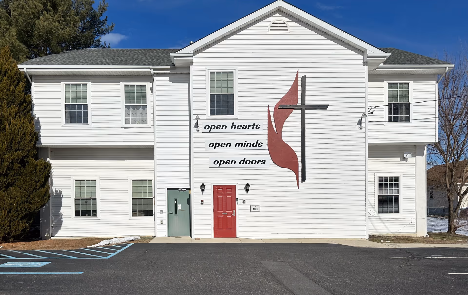 A white two-story senior care building with a cross logo and 'open hearts' slogan.
