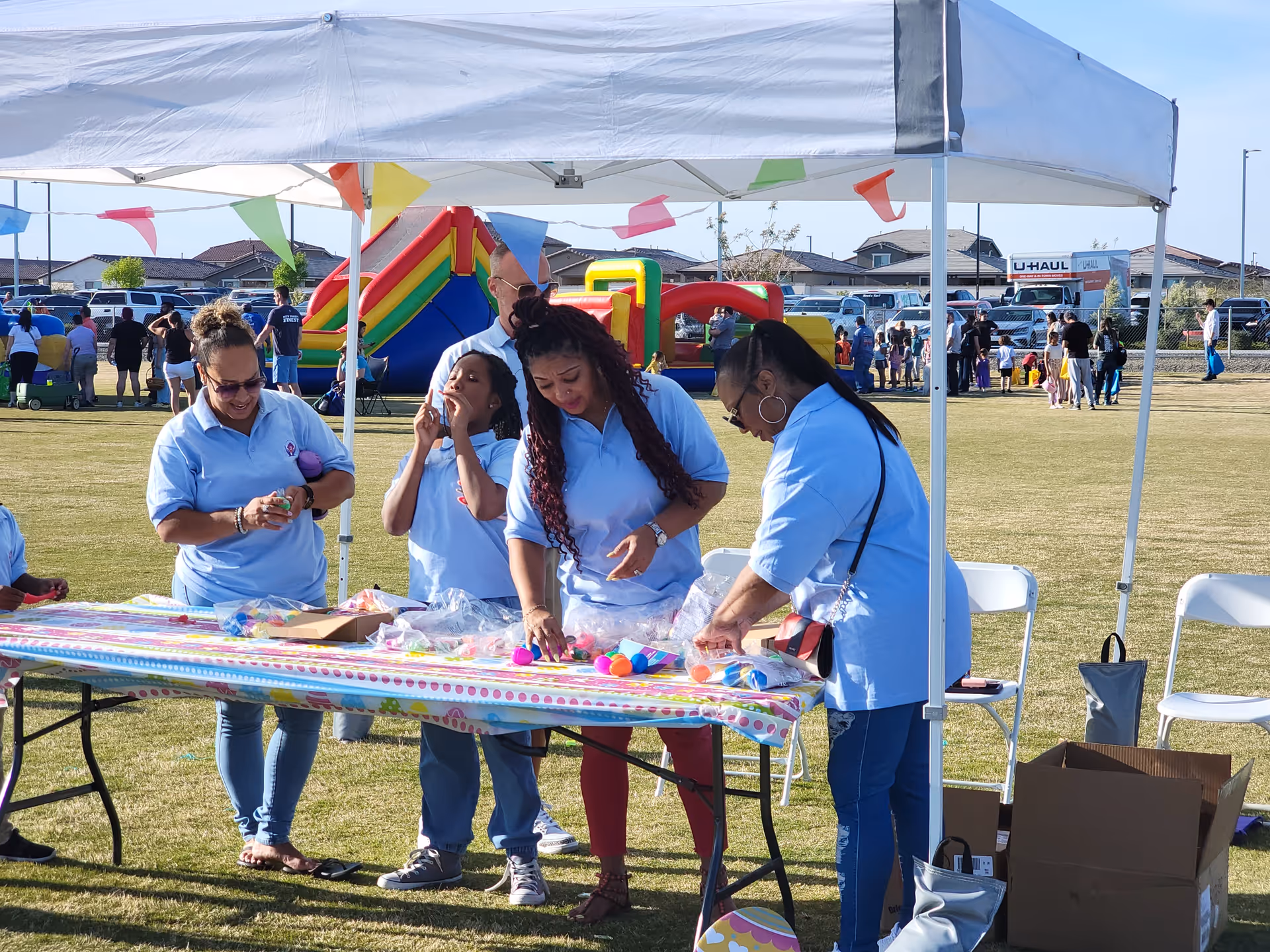 Caregivers in light blue shirts run crafts at an outdoor event under a white canopy.