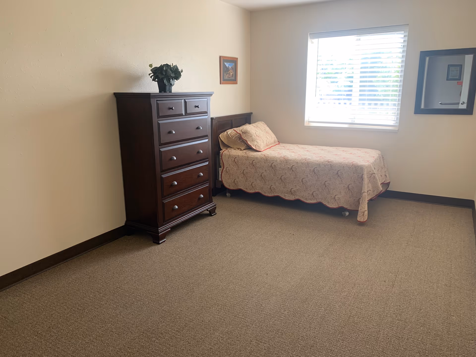 A simple bedroom with a bed, dresser, window, and framed artwork.