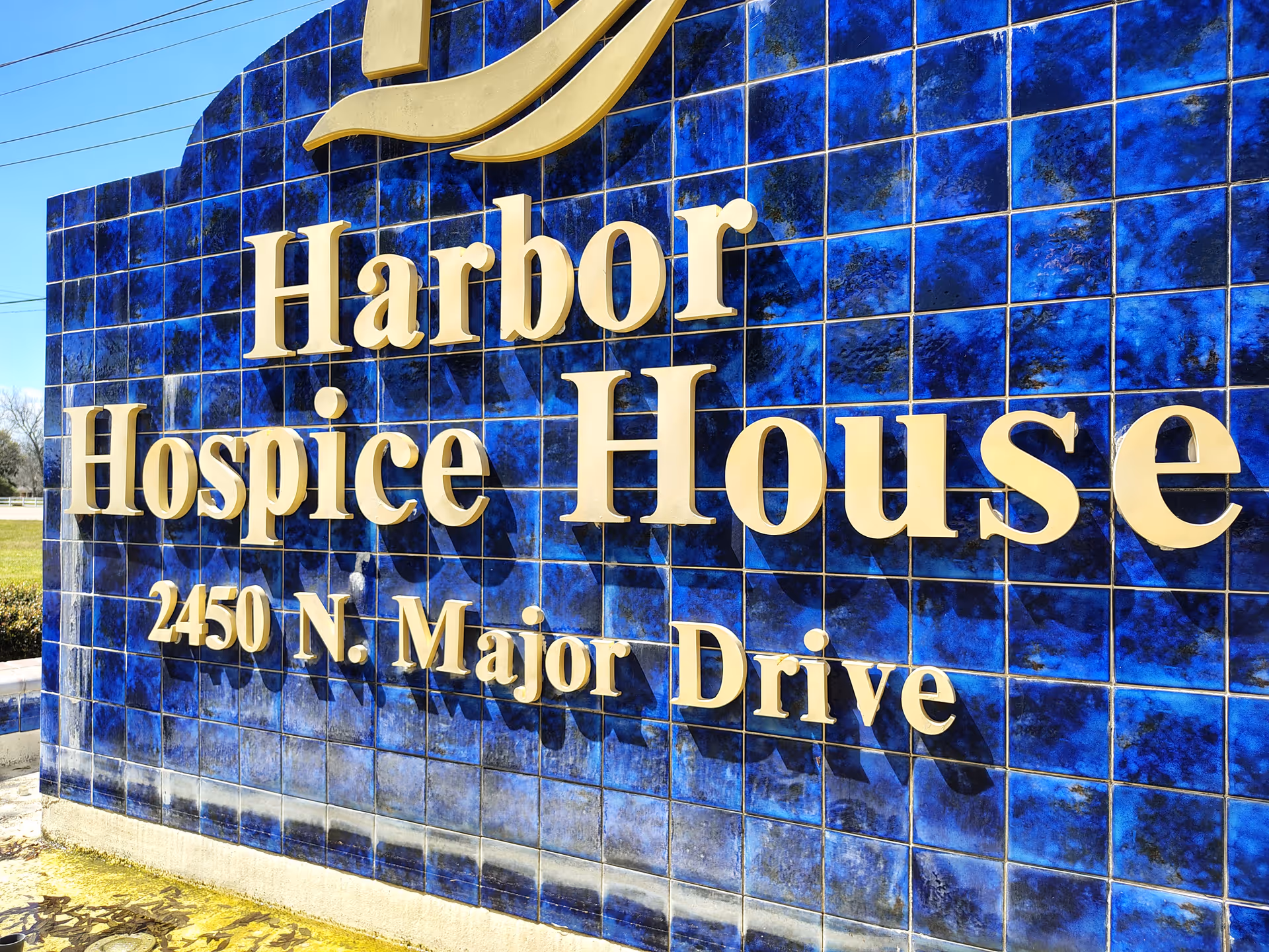 Blue tiled exterior sign reading Harbor Hospice House and address on front wall.