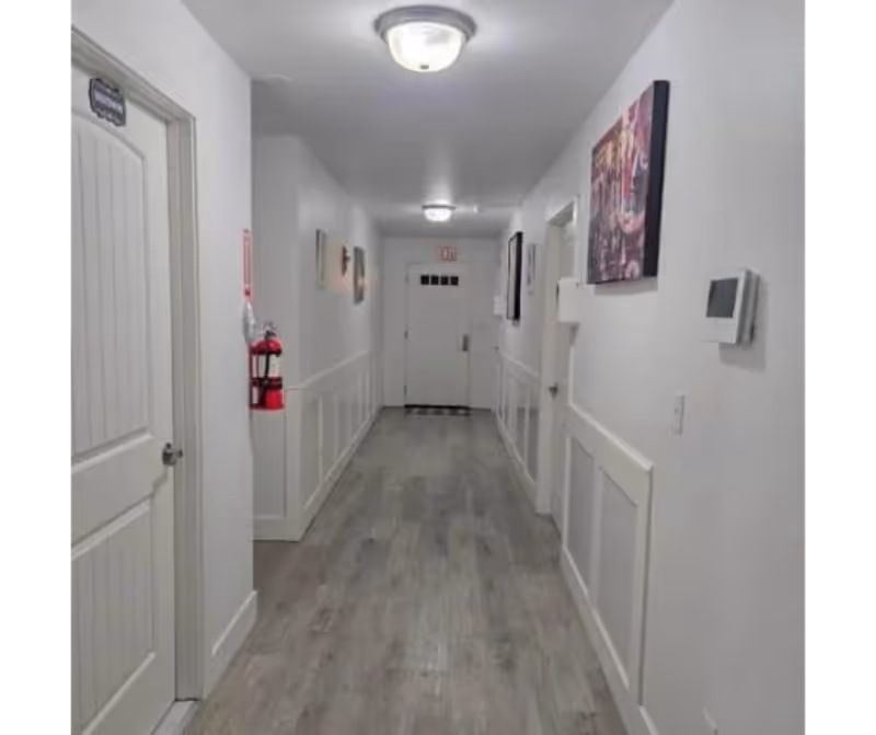 Long white hallway in a senior living facility with doors and artwork.