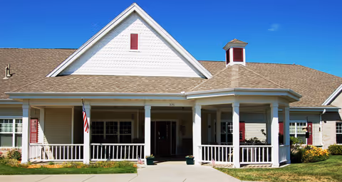 Front view of a single-story senior living facility with a porch, columns, and an American flag.