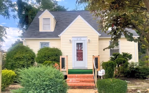 Front exterior of a yellow cottage-style assisted living facility with steps and greenery