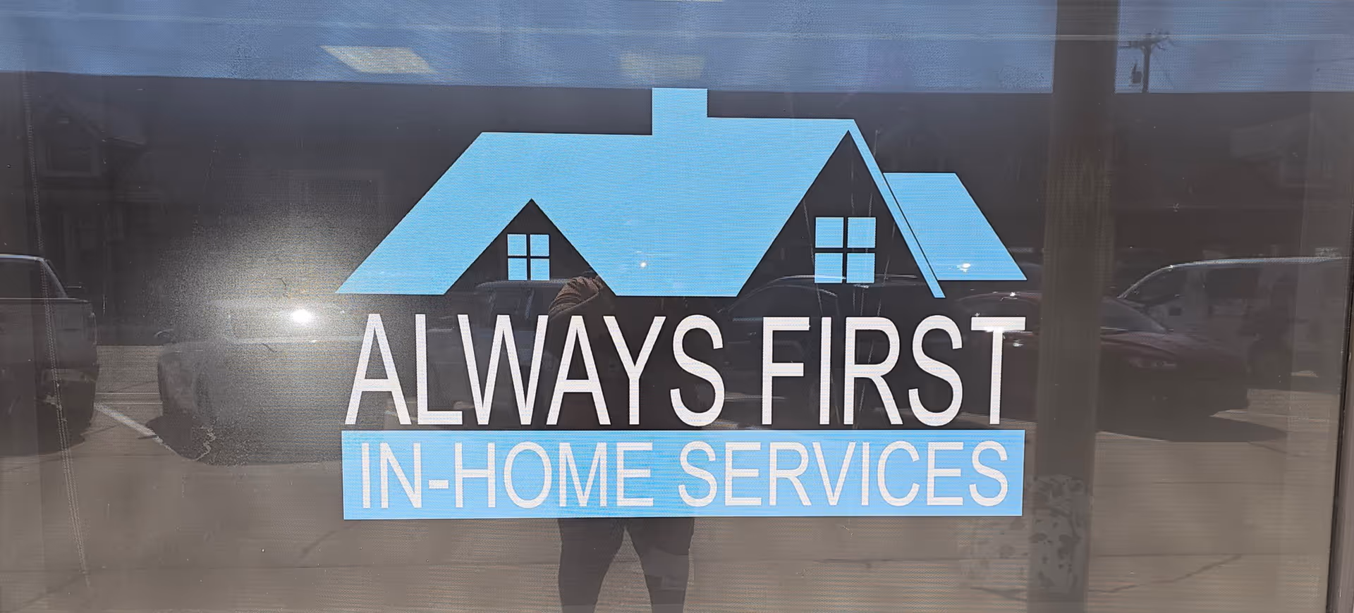 Glass storefront window displaying the Always First In-Home Services logo with photographer reflection.