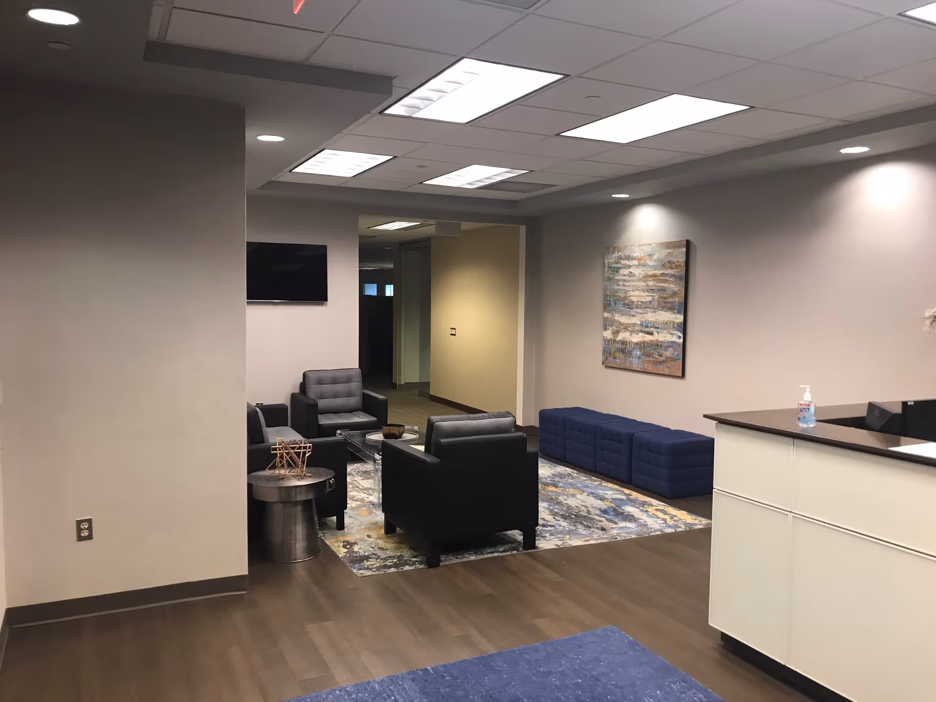 Modern lounge area with black chairs, blue ottomans, and a reception desk.