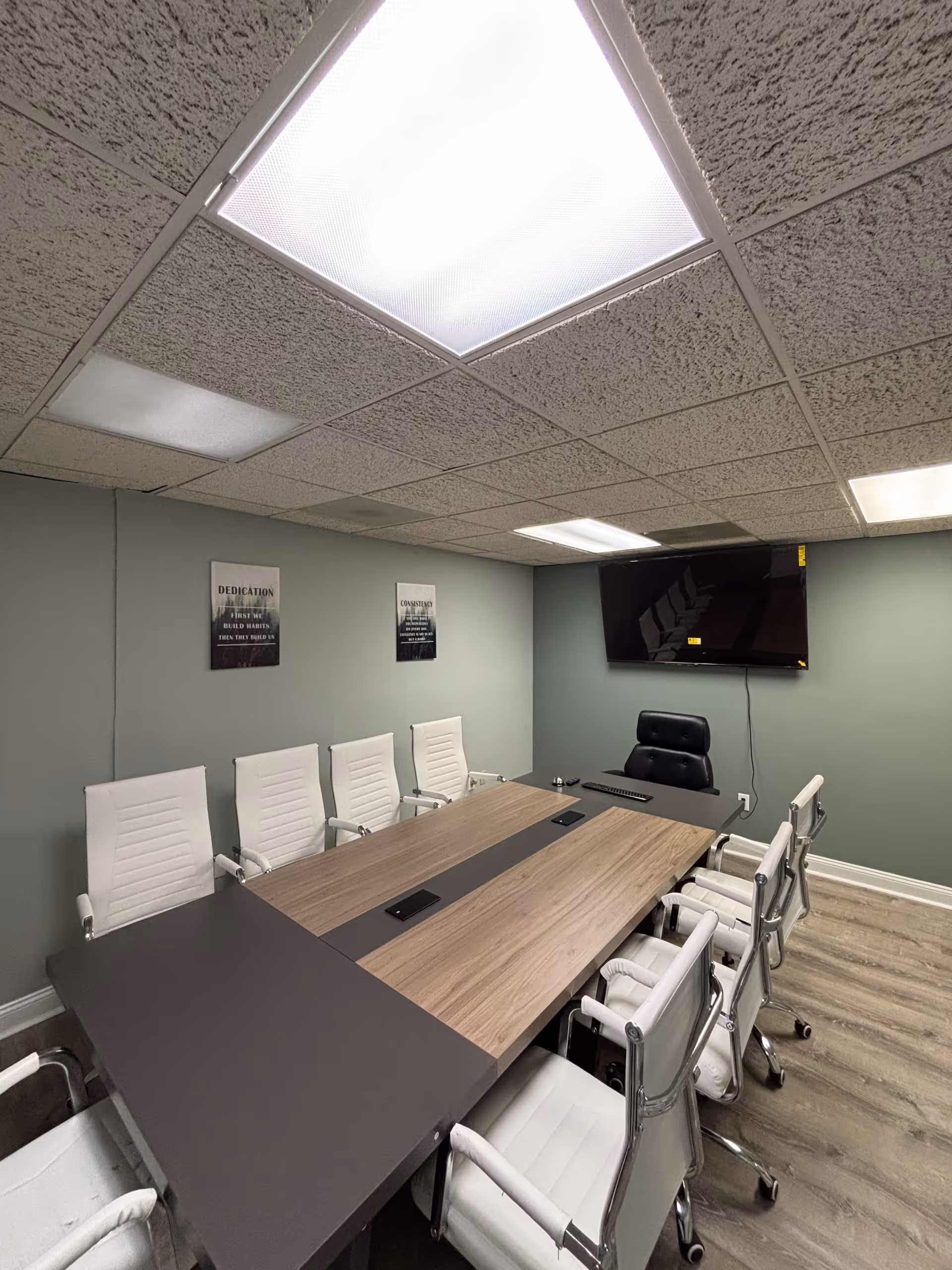 Modern conference room with a long table, white chairs, and wall-mounted TV.