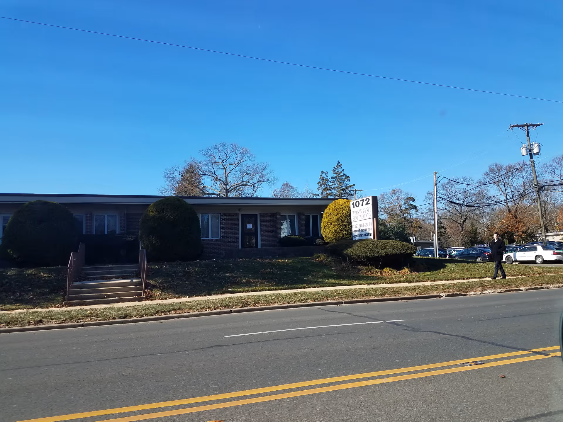 Front view of a single-story senior care building with landscaping and a sign.