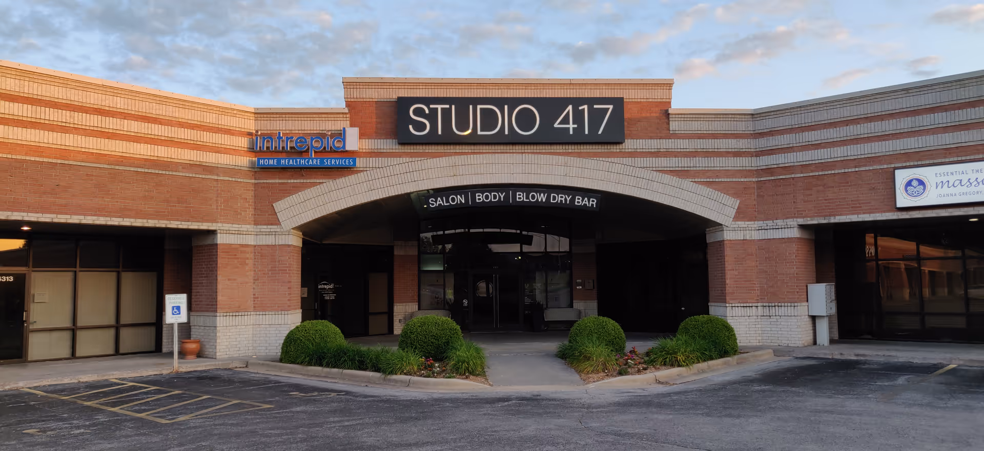 Brick storefront with Studio 417 sign and Intrepid branding, curved entrance, and trimmed shrubs in front.