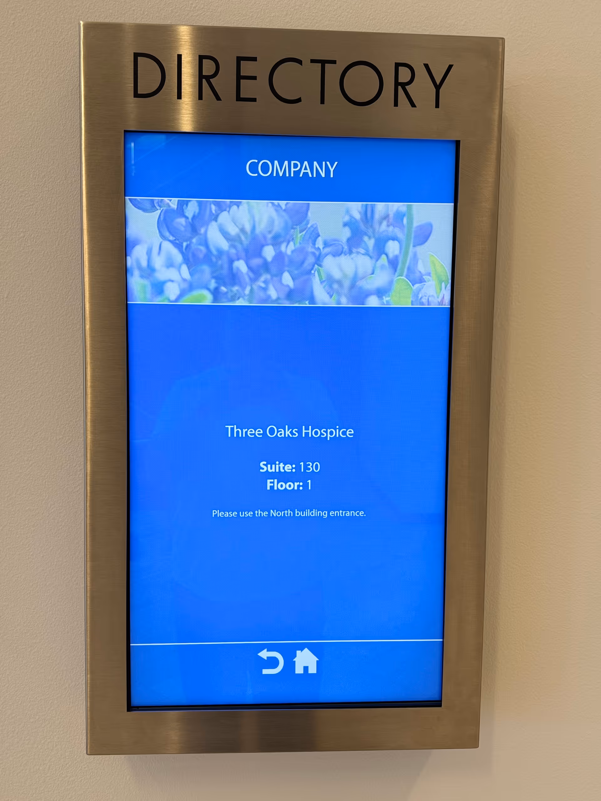 Metal framed digital directory screen mounted on a wall showing Three Oaks Hospice information.