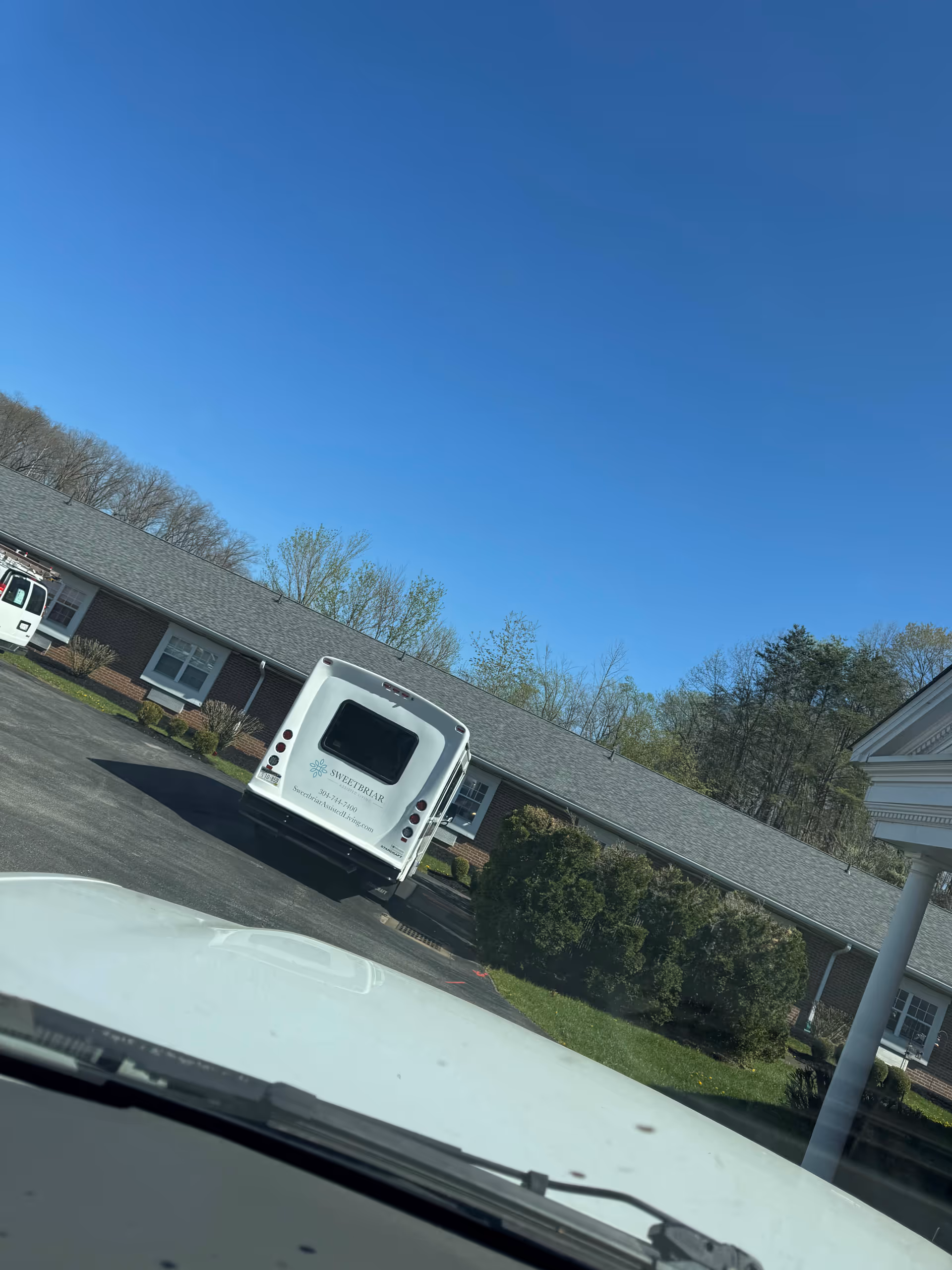 White bus with SweetBriar logo parked in front of a single-story brick assisted living facility.