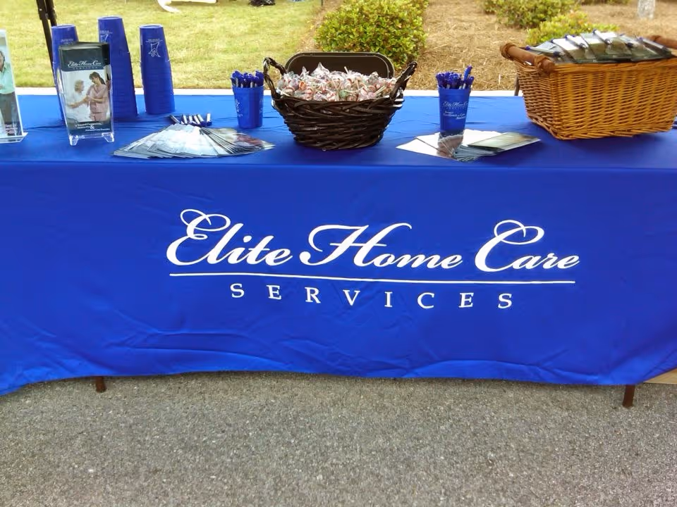Outdoor table display with blue Elite Home Care Services branding, brochures, and baskets.