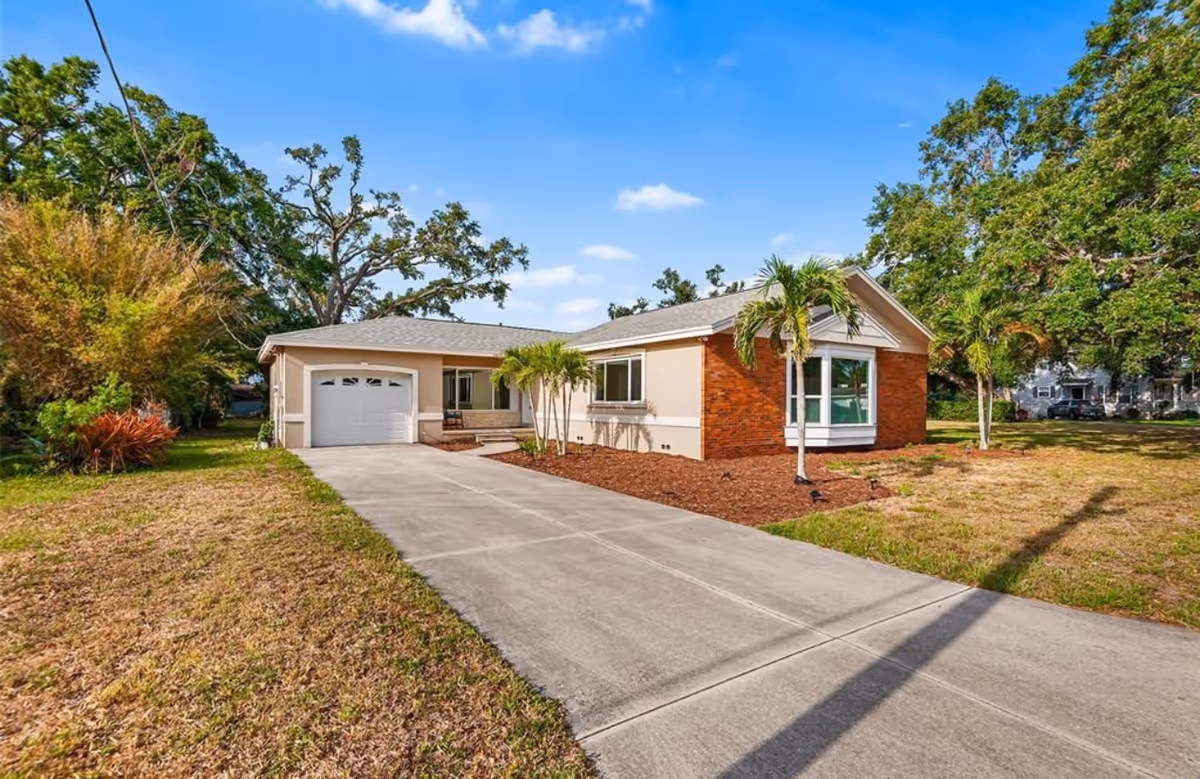 Front view of a single-story building with driveway, palm trees, and brick accents.