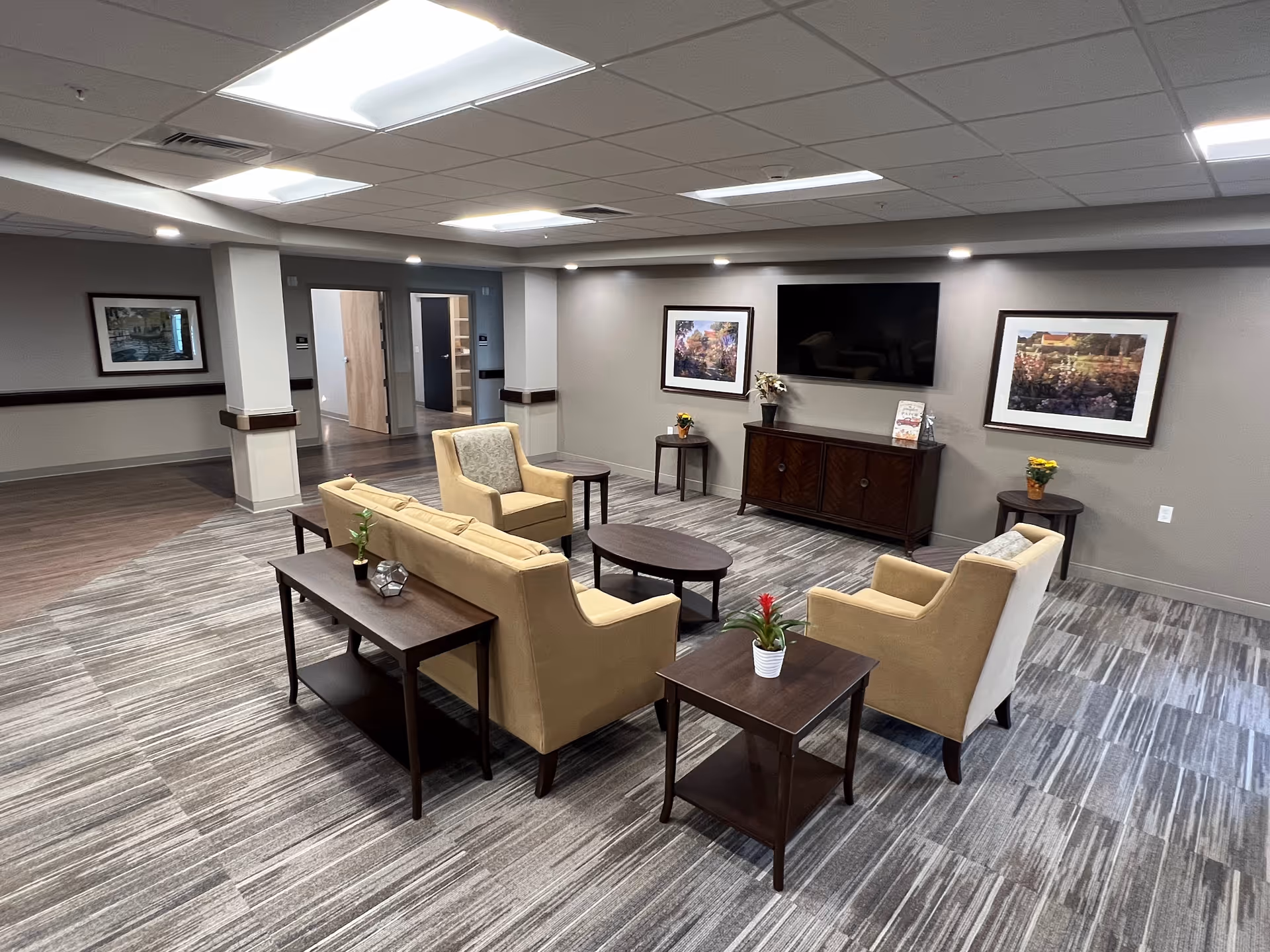 Spacious lounge with beige seating, dark wood tables, framed art, and wall-mounted TV.