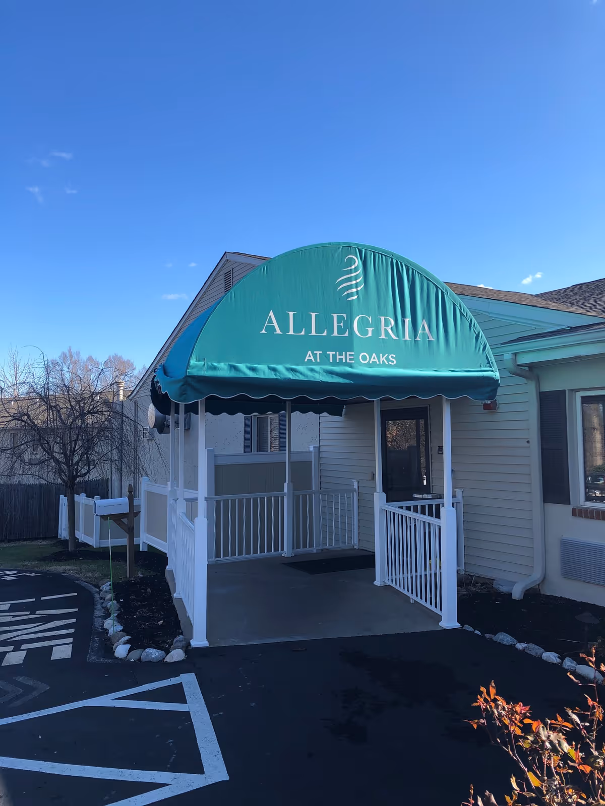 Entrance of Allegria at The Oaks with a teal canopy over a ramped porch and white railings.