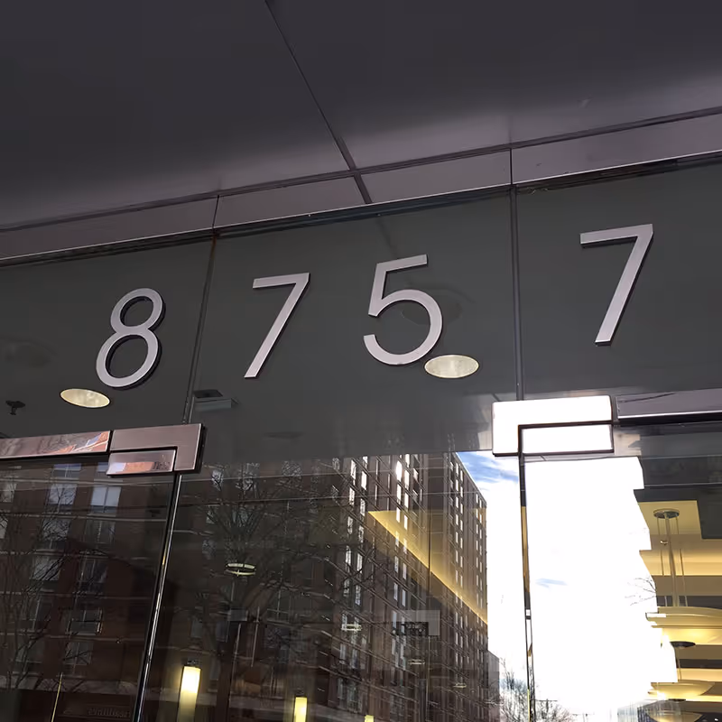 Glass entrance with large numbers 8 7 5 7 and reflections of surrounding buildings.