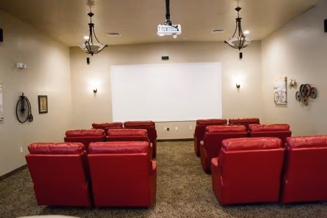 Red upholstered chairs face a white projection screen in a small indoor theater room.