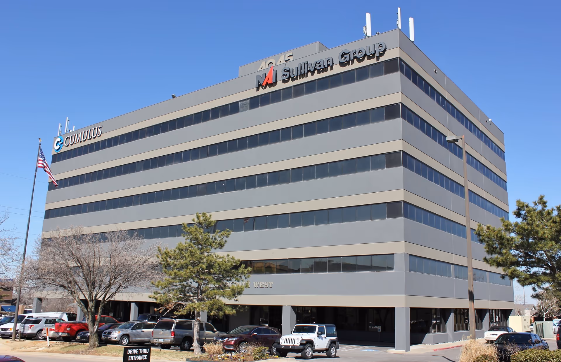 Modern, multi-story office building with horizontal bands and a parking lot.