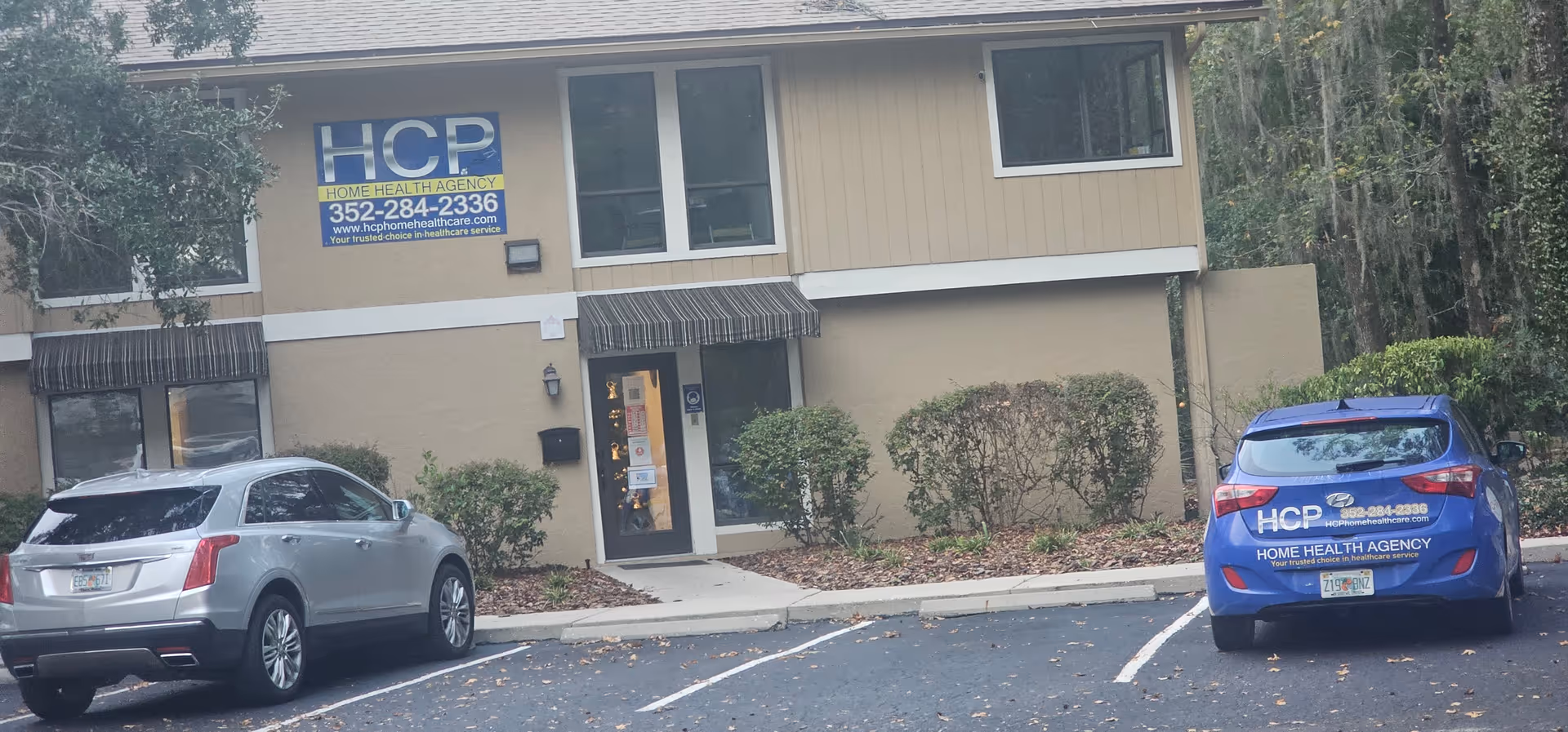 Front view of beige building with HCP sign, entrance, and two parked cars.