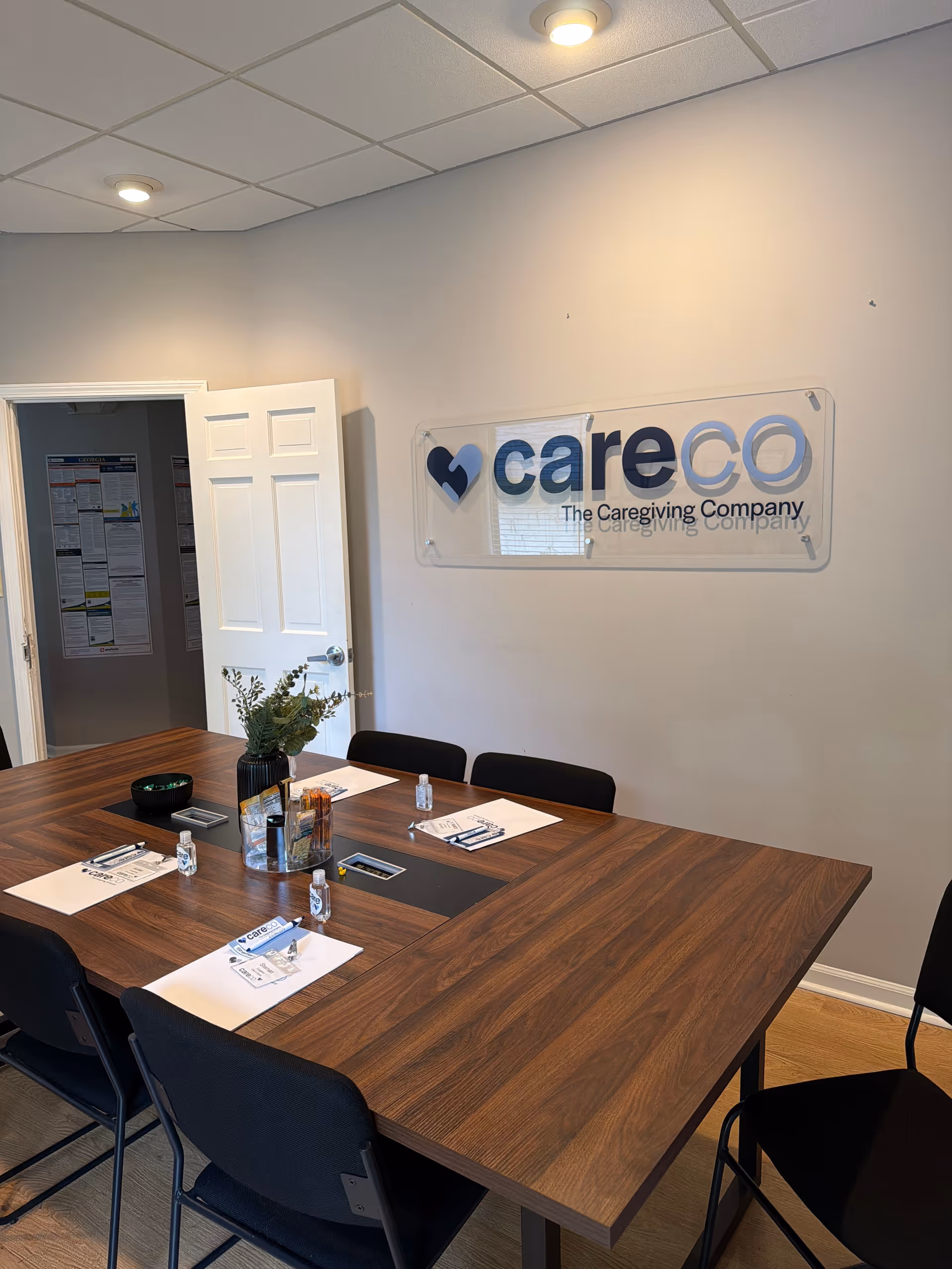Conference room with a wooden table, black chairs, and a CareCo sign on the wall.