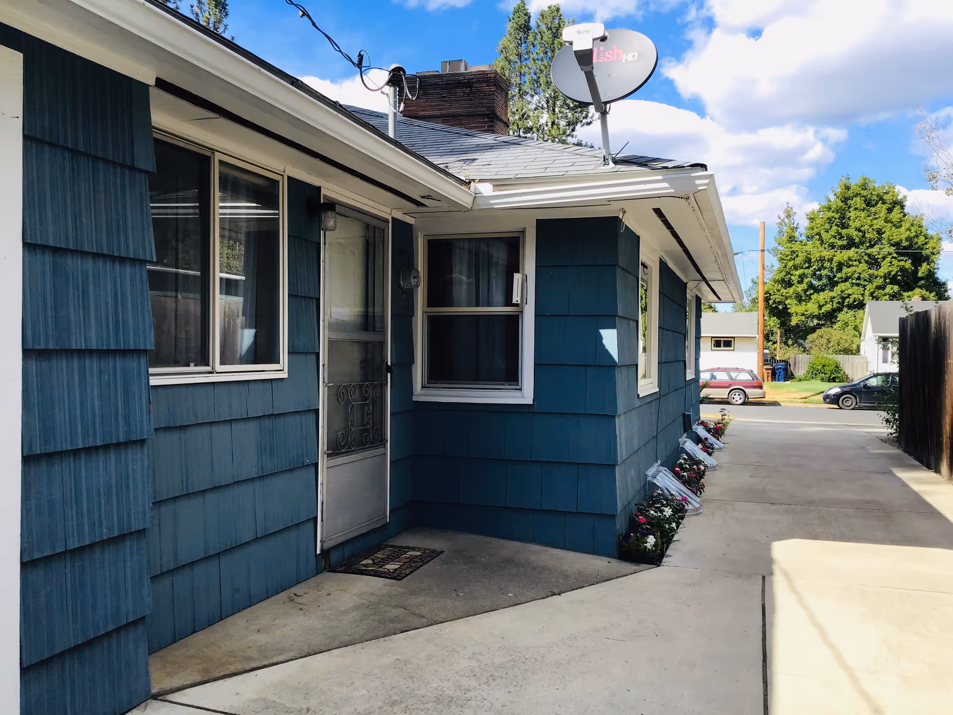 Blue single-story home exterior with a walkway and flower planters along the wall.