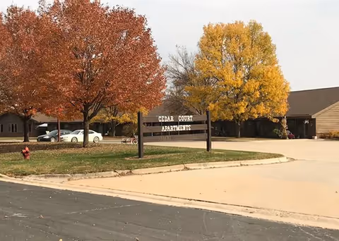Exterior view of a senior living facility with Cedar Court Apartments sign and autumn trees.
