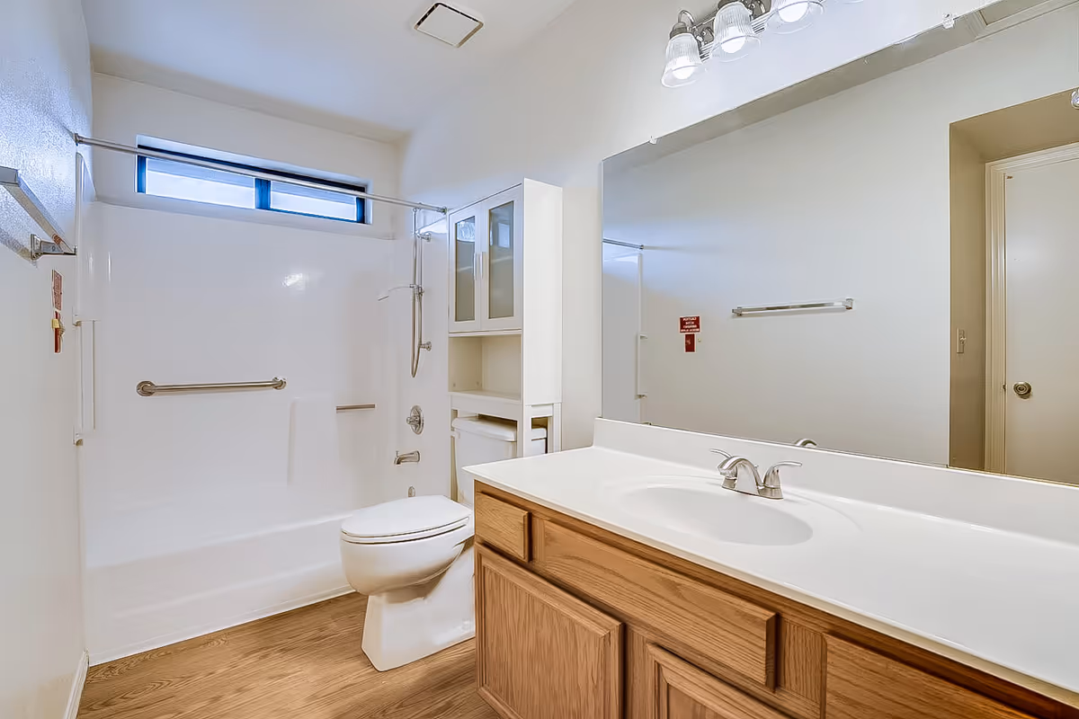 Bright bathroom with sink, toilet, and accessible shower in a senior living facility