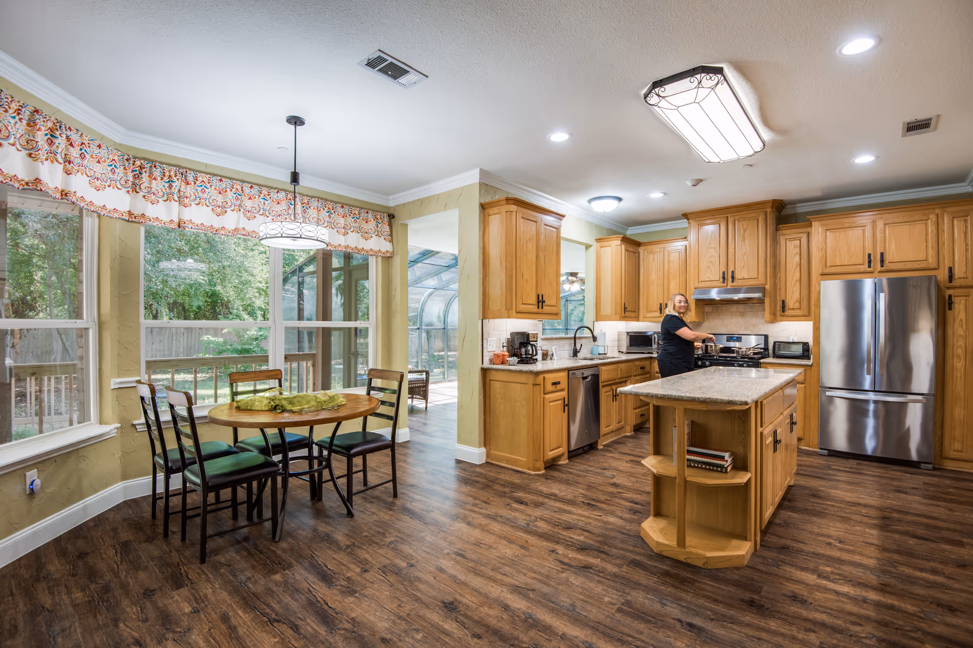 Bright kitchen with wooden cabinets, island, stainless fridge, and a person cooking.