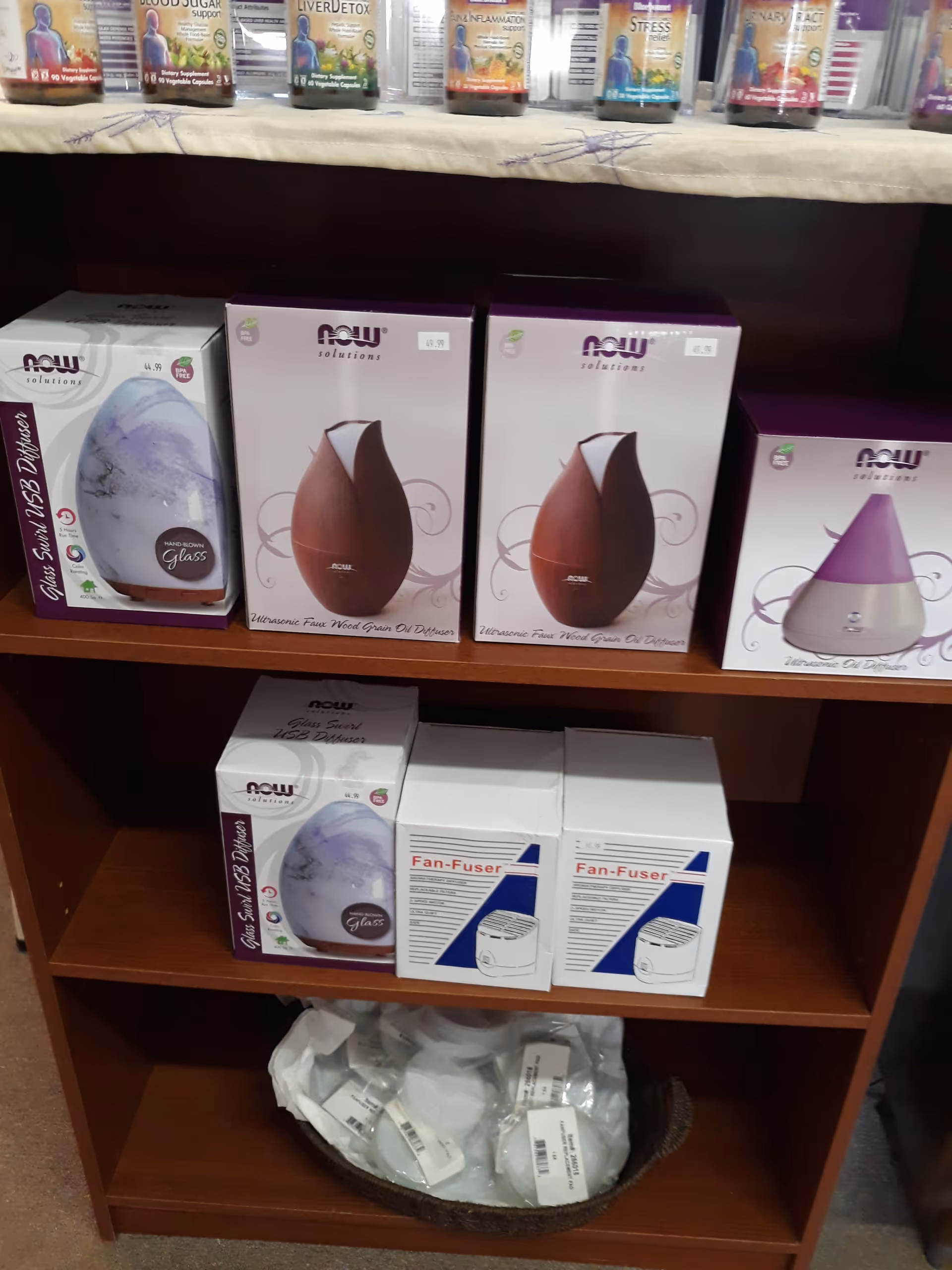 Wooden display shelf filled with Now Solutions product boxes and a bottom plastic bag.
