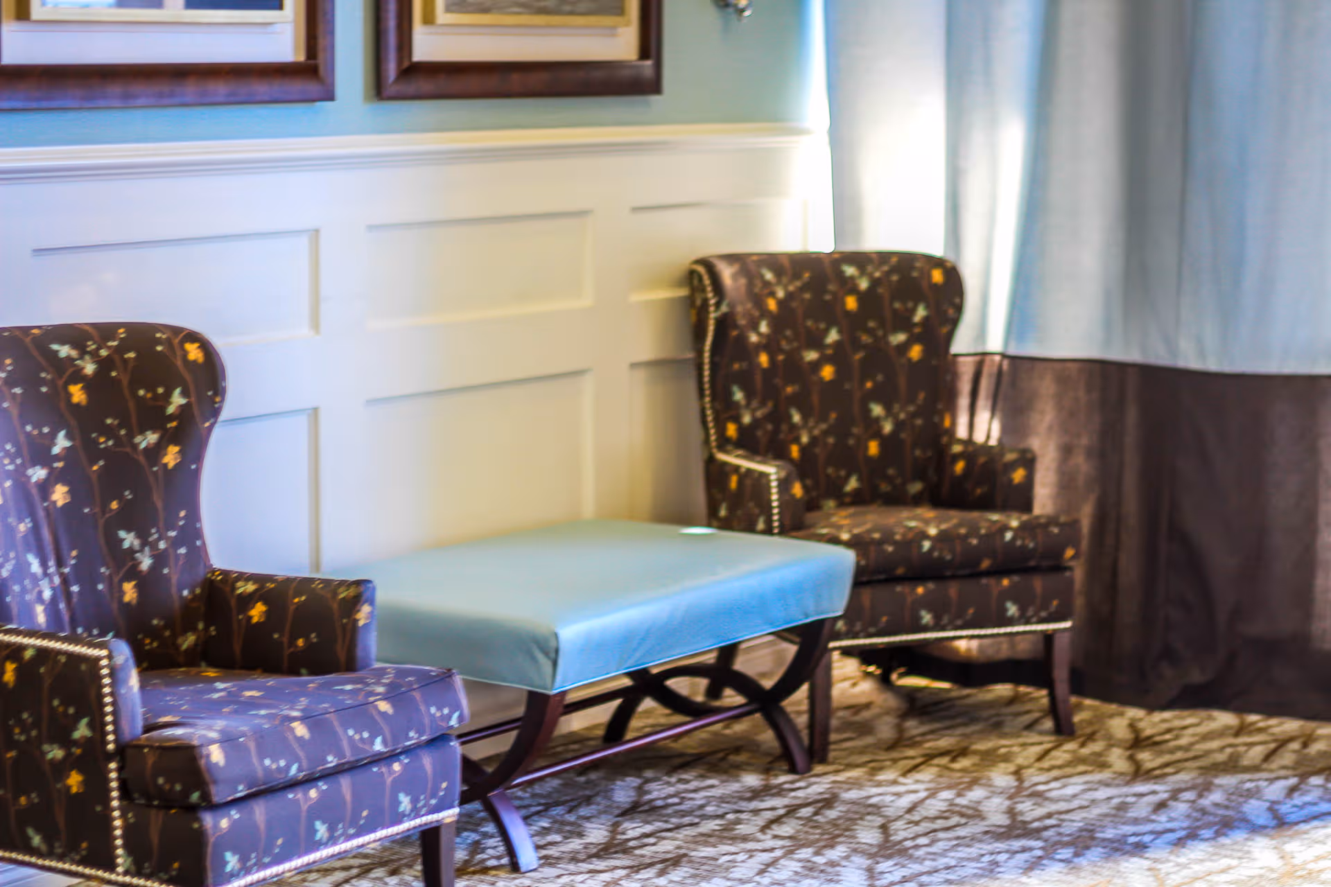 Two floral upholstered chairs flank a blue cushioned ottoman in a living room lounge.