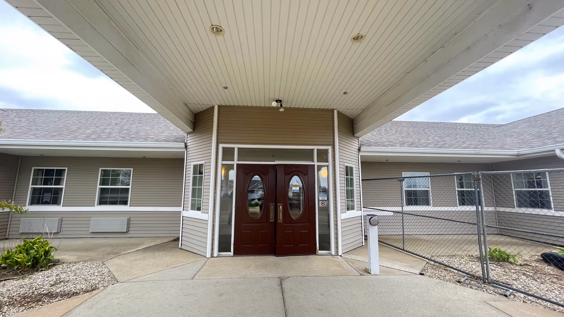 Front entrance of a single-story senior living facility with double wooden doors under a covered entry.