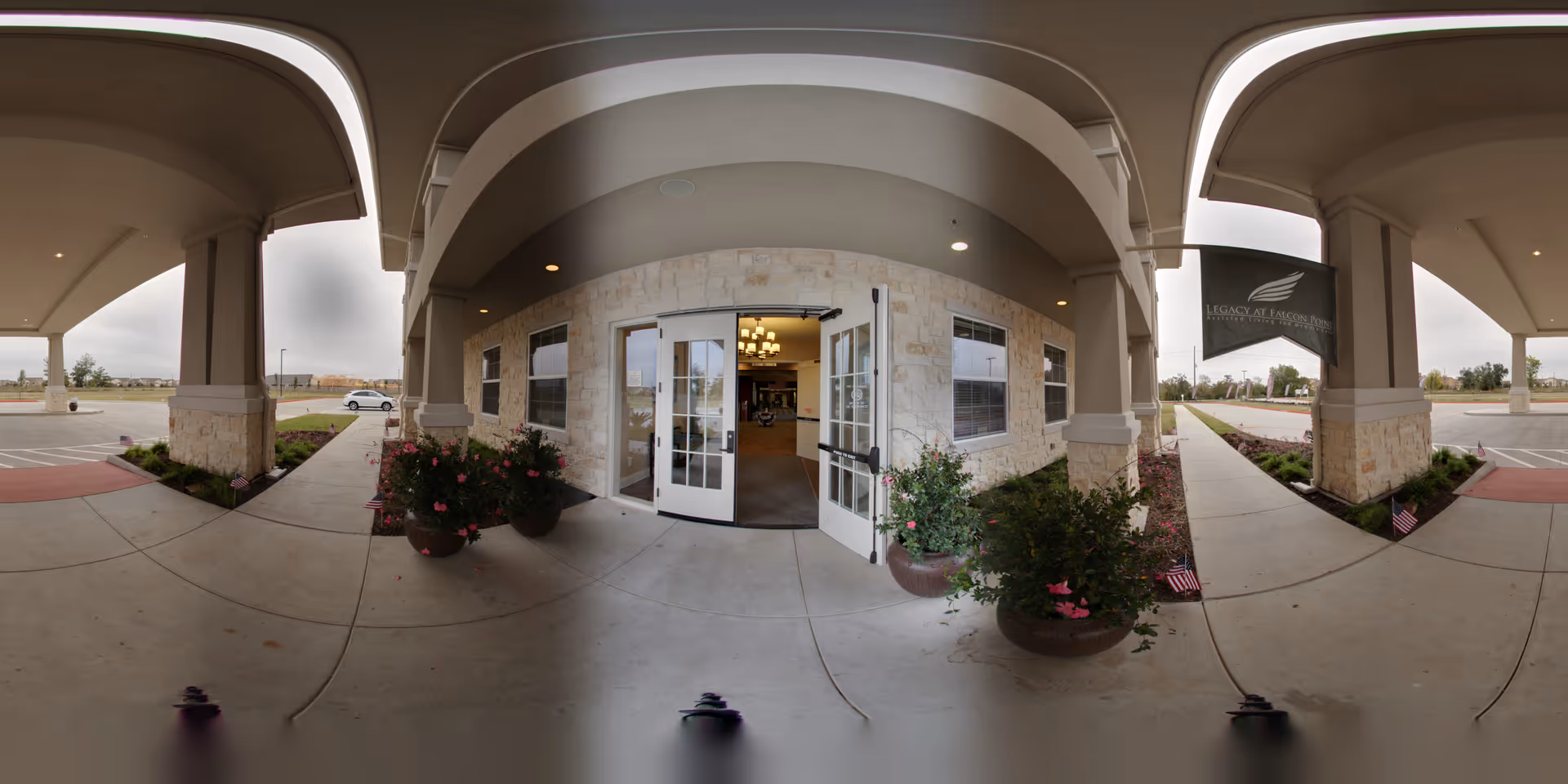 Covered porte-cochere and main entrance of The Legacy at Falcon Point with double glass doors, stone facade, and potted flowers.