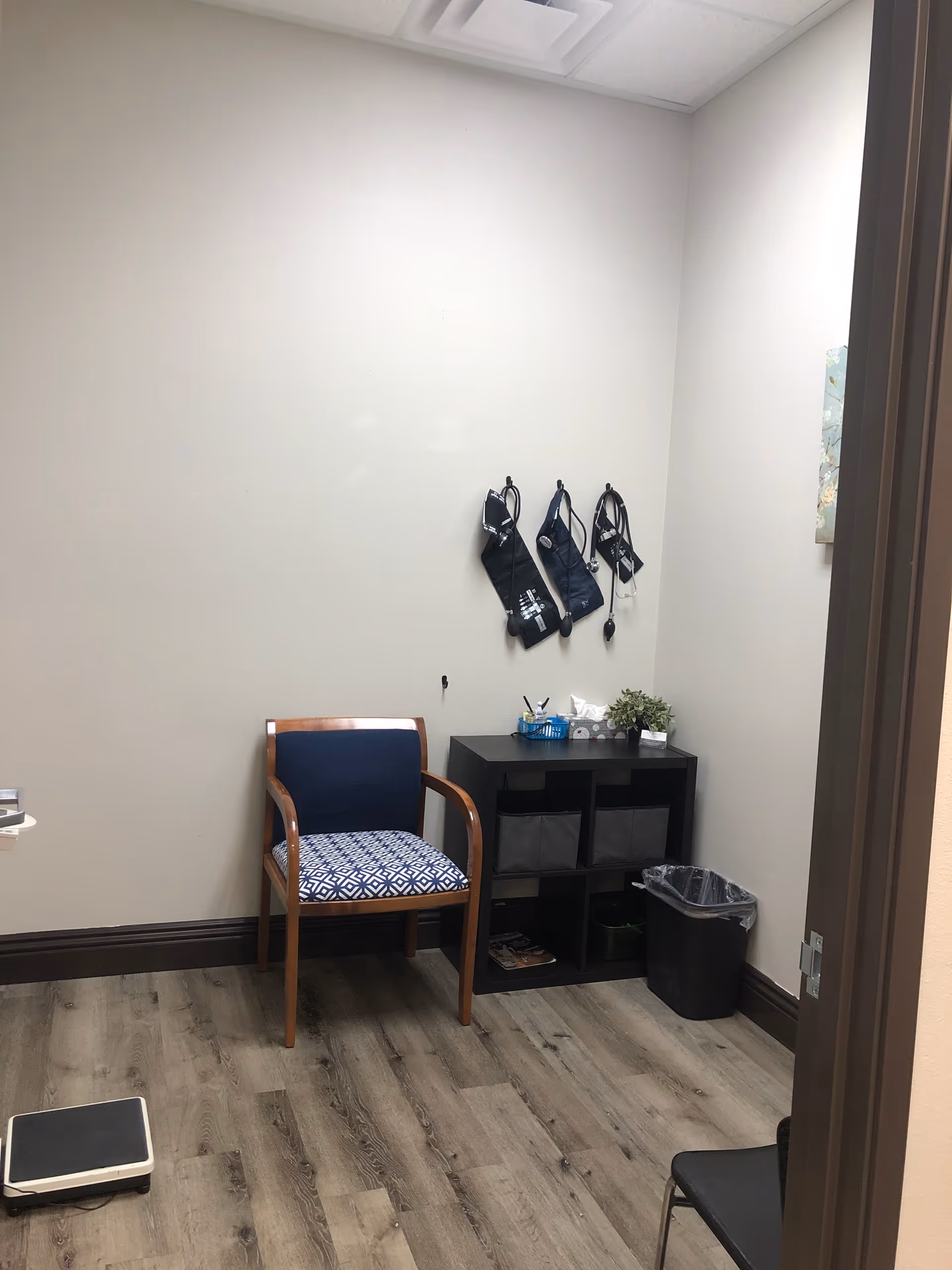 Small neutral room with chair, storage cabinet, hooks for bags, and a scale.