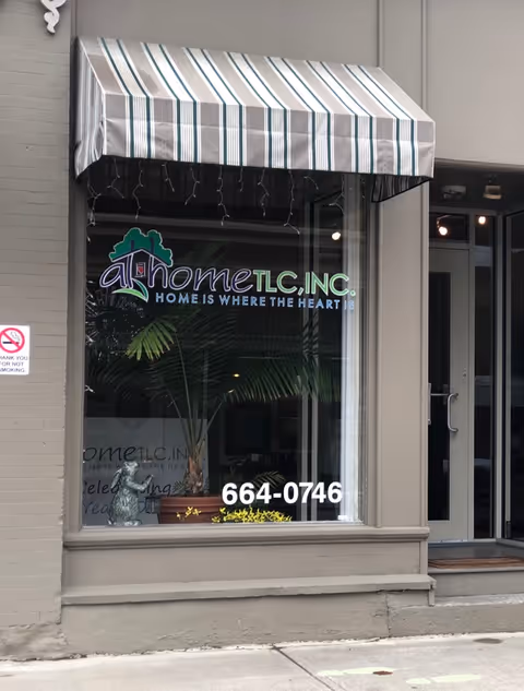 Storefront of At Home TLC, Inc. with striped awning, glass window, and entry door.