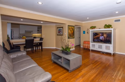 Spacious living area with beige walls, wood floors, couch, coffee table, and TV.
