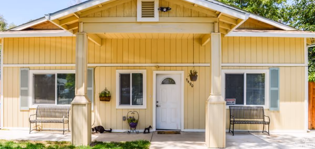 Beige residential building with a covered front porch, two benches, and a central white door.