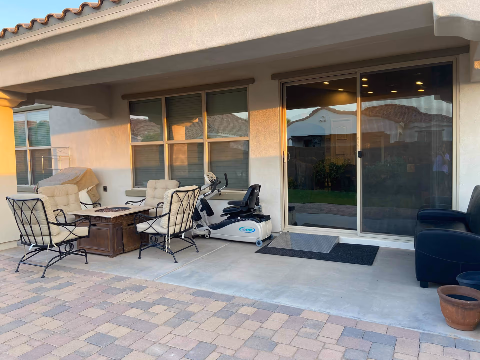 Patio with cushioned chairs around a fire pit table and exercise equipment near a sliding door.