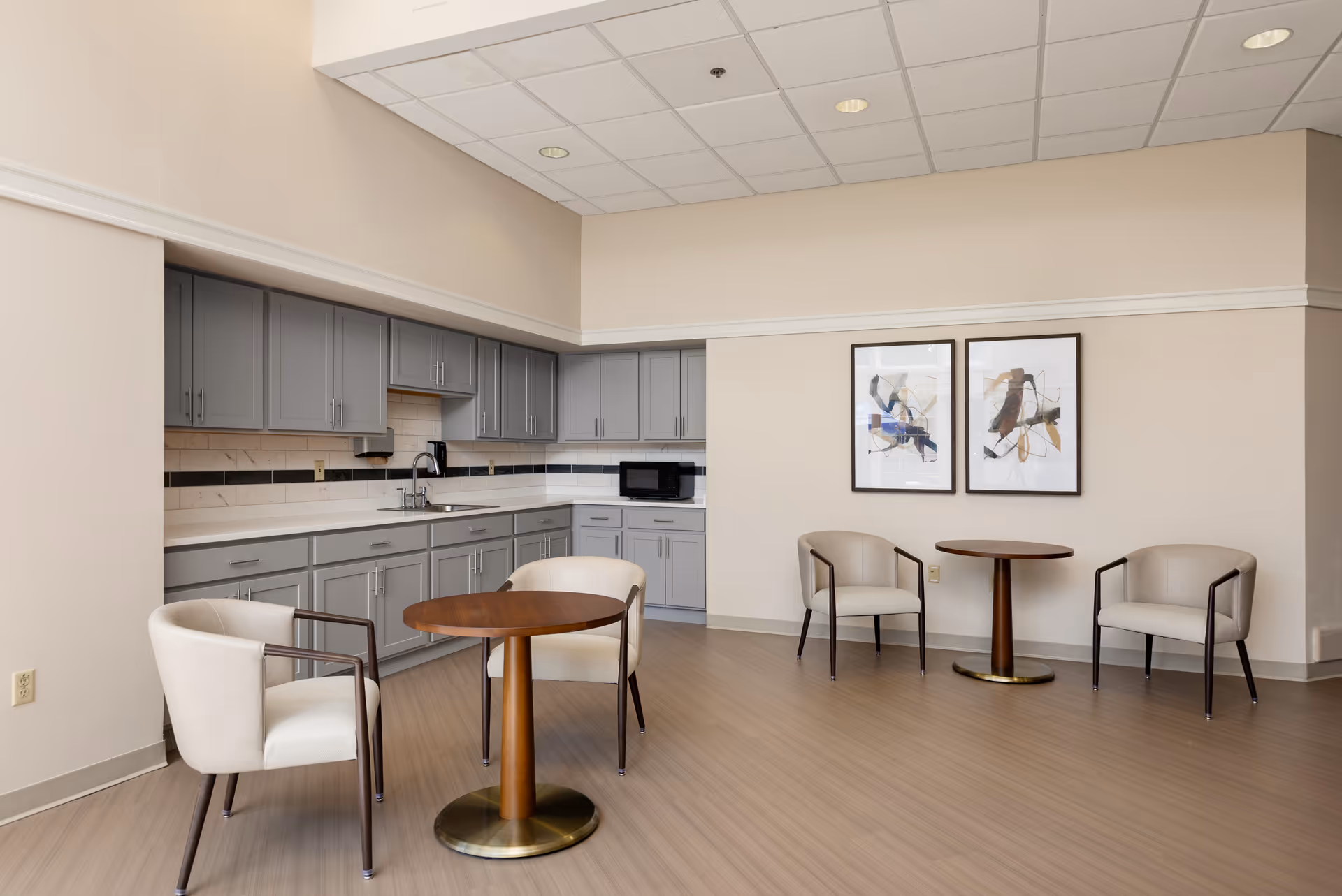 Compact kitchenette with gray cabinets and small seating area in a neutral, modern lounge.